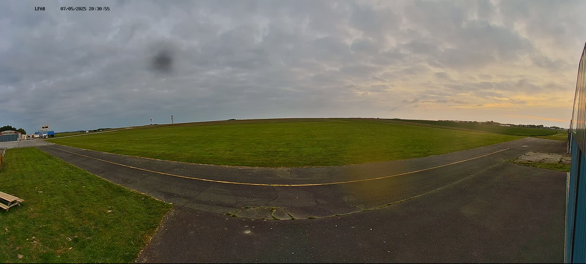A paved taxiway curves through a grassy airfield under a mostly cloudy sky with a hint of sunset.