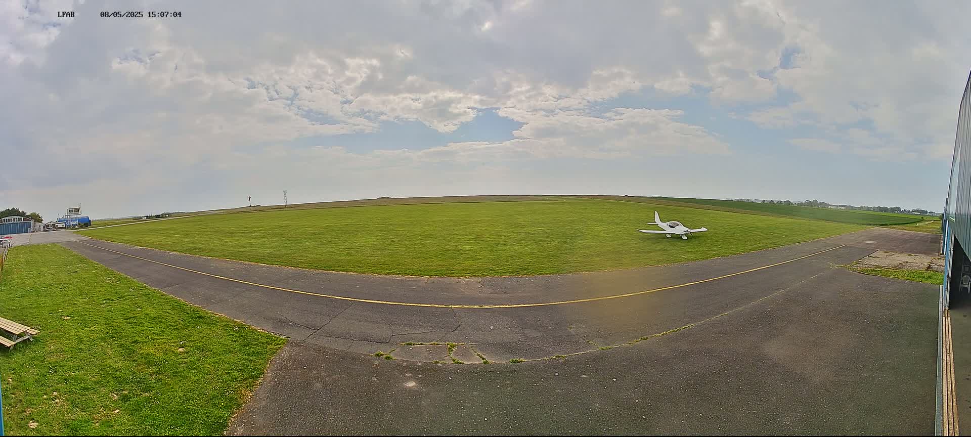 A small, white airplane sits on a grassy airfield under a partly cloudy sky.