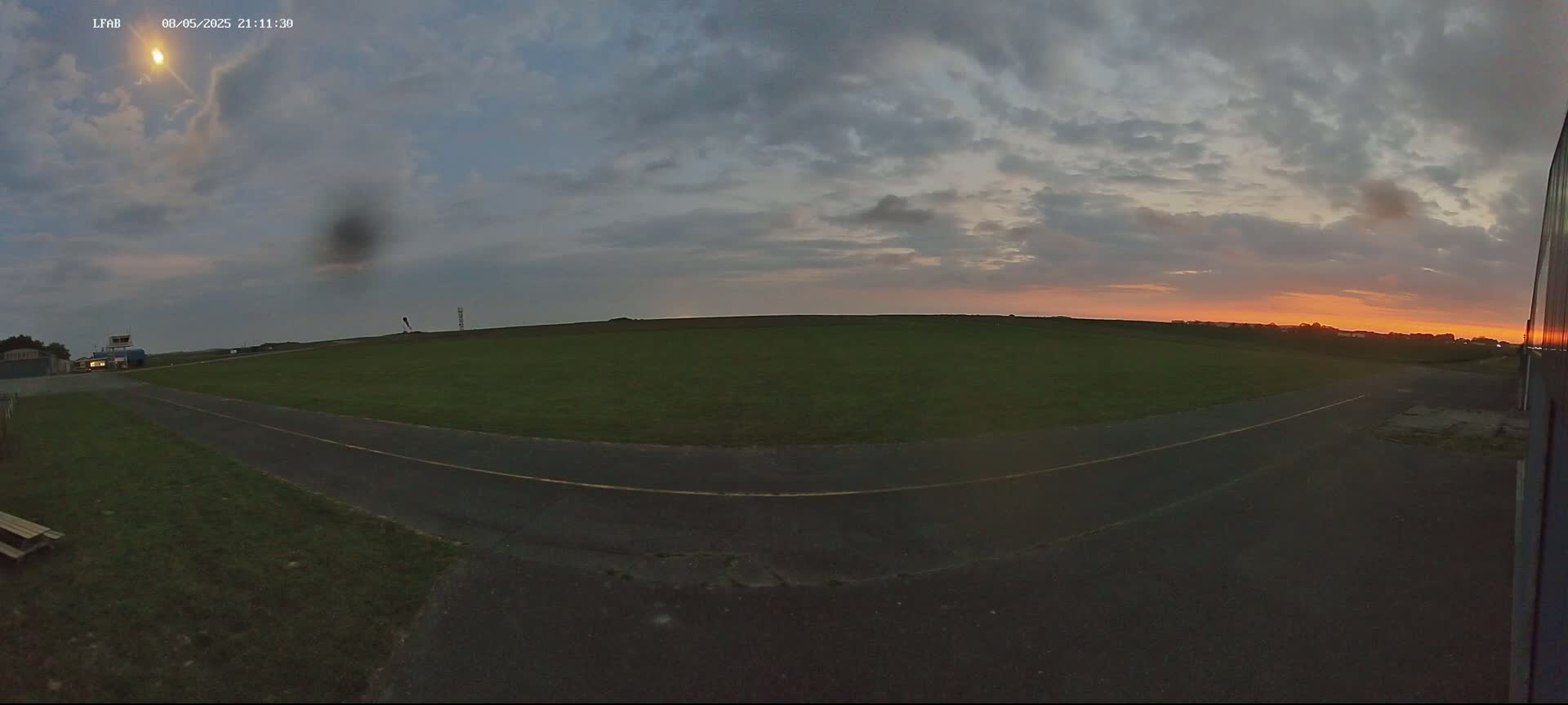 A paved path curves through a grassy airfield during a cloudy sunset.