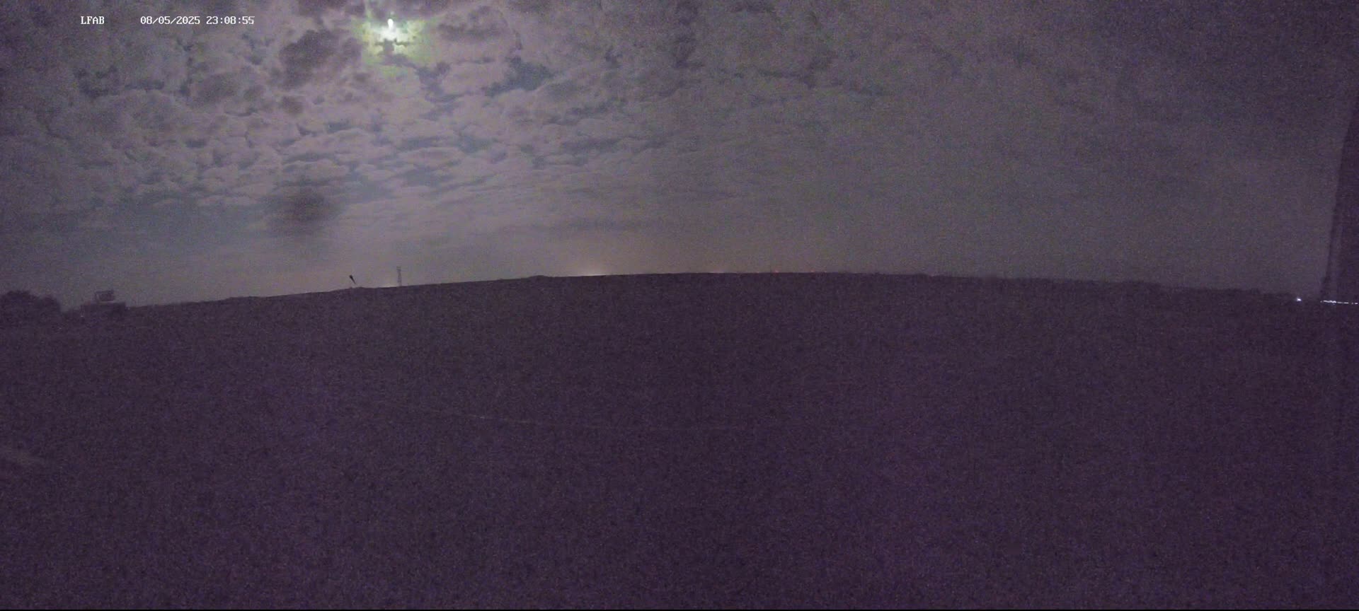 A moonlit night sky with scattered clouds is visible above a dark, flat landscape.