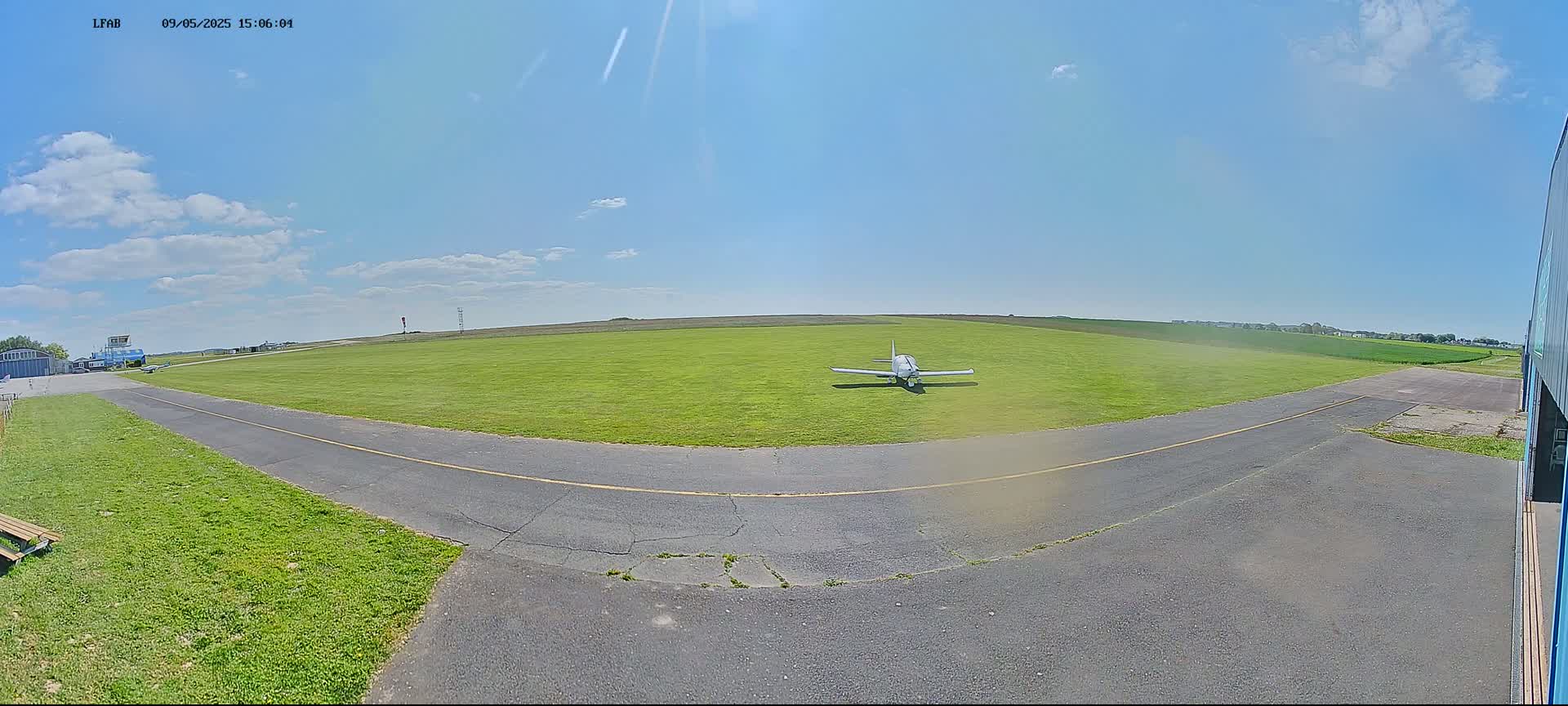 A small airplane sits on a grassy airfield under a mostly sunny sky.