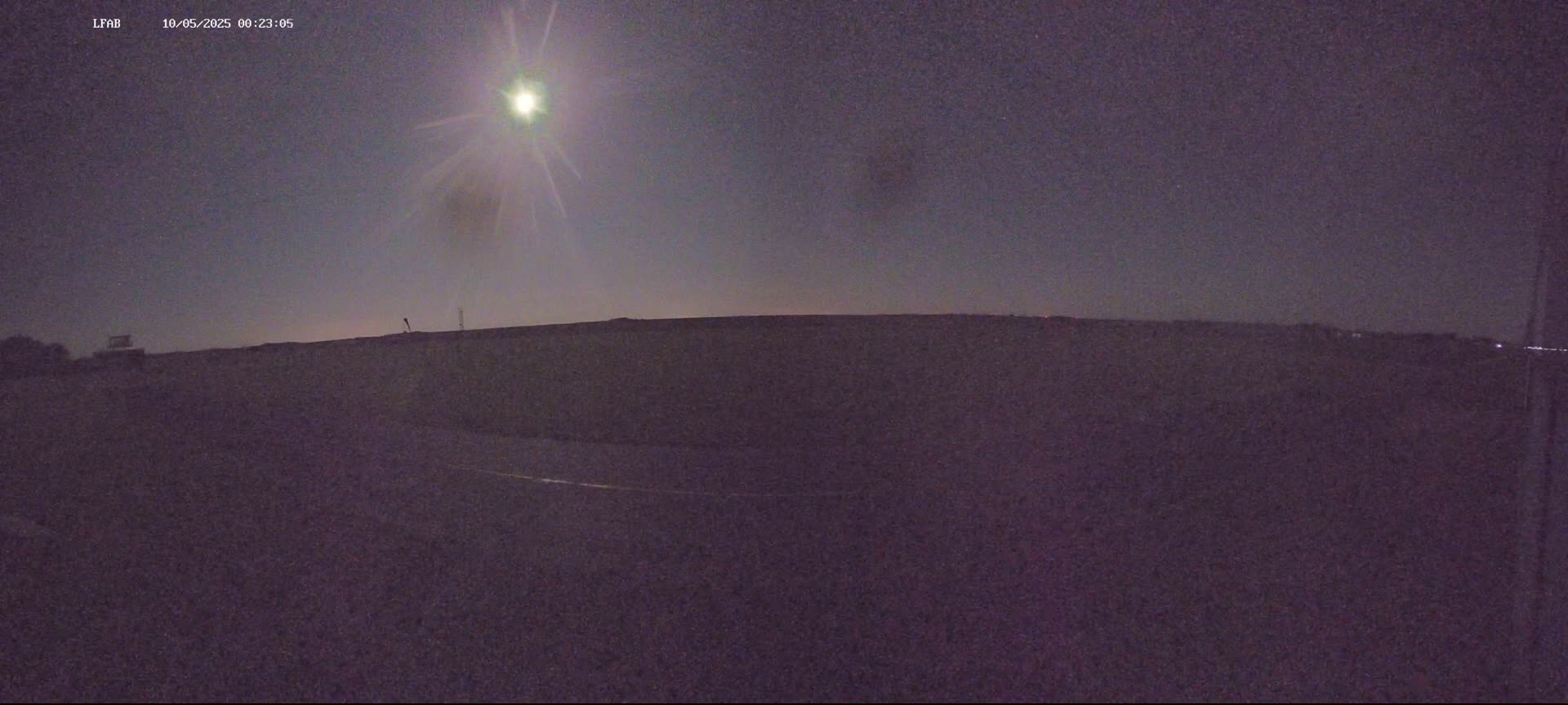 A bright moon shines in a dark, night sky over a flat, dark landscape.