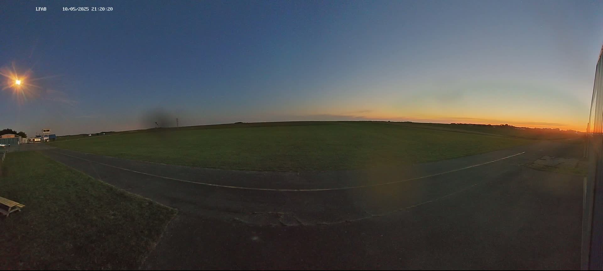 A paved area next to a grassy field at sunset under a clear, twilight sky.