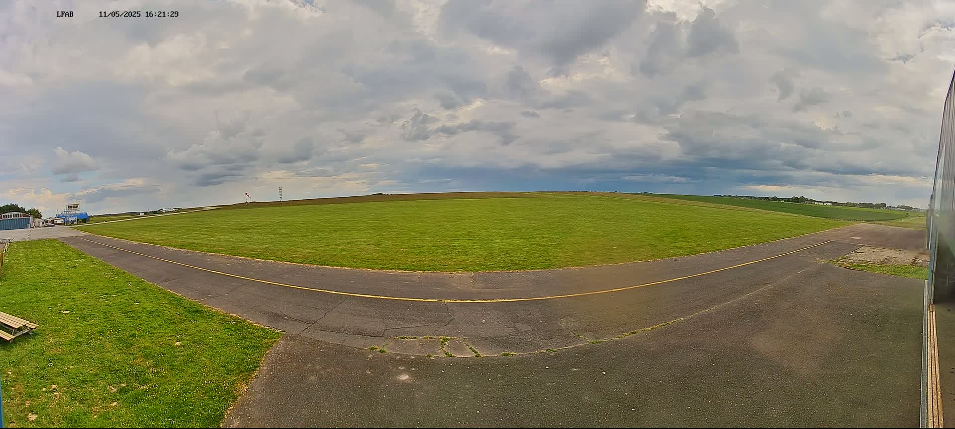A grassy airfield with a paved taxiway is visible under a partly cloudy sky.
