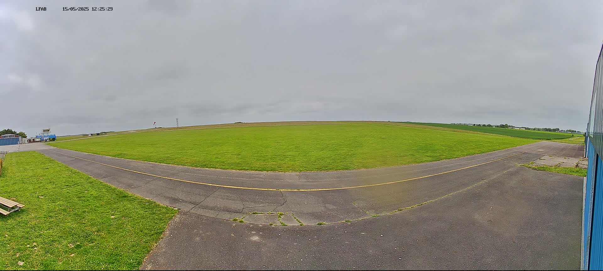 A grassy airfield with a paved taxiway curves to the left under an overcast sky.