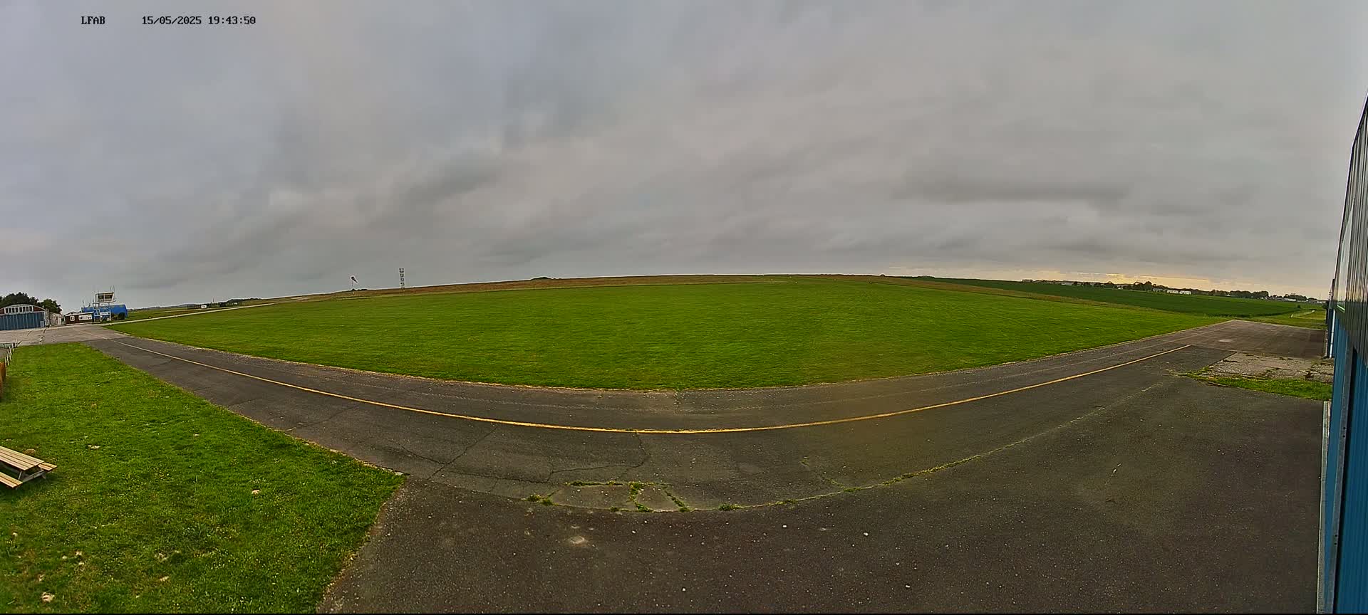 A grassy airfield with a paved taxiway under an overcast sky.