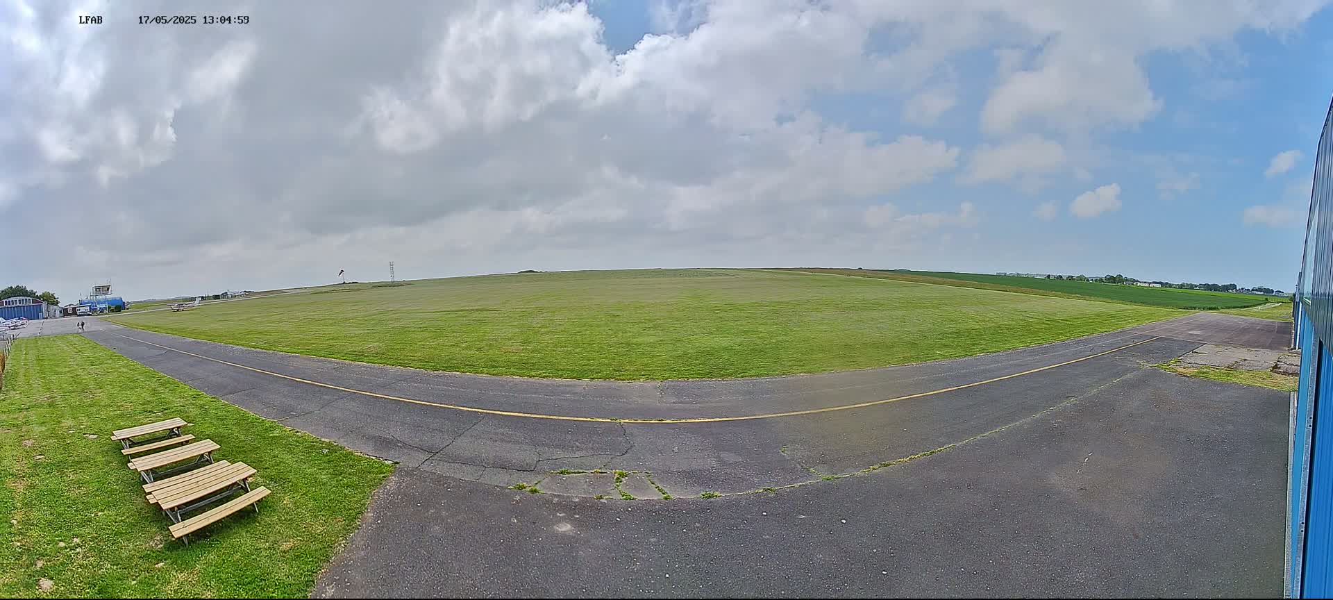 A grassy airfield with a paved taxiway is visible under a partly cloudy sky.