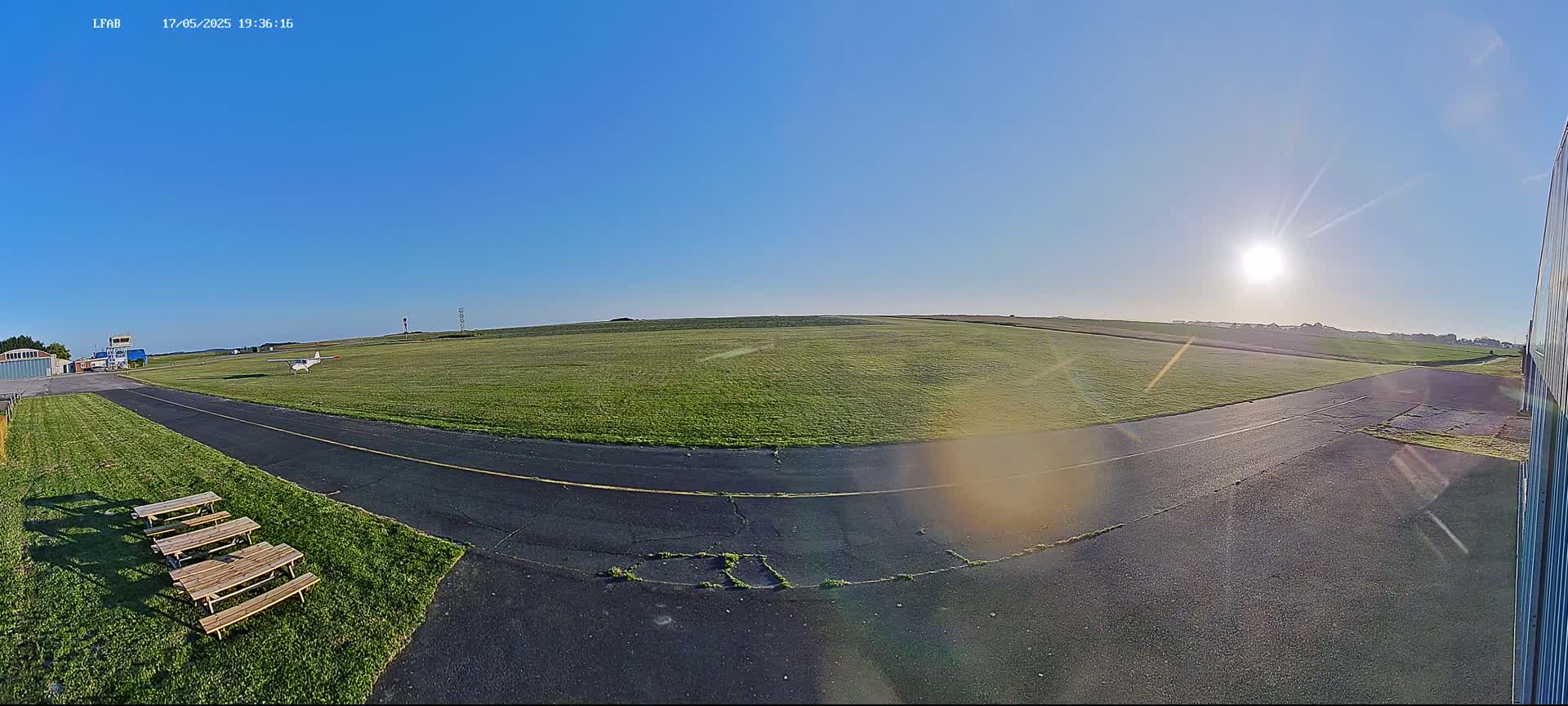 A small airplane sits on a grassy airfield under a bright, sunny sky.