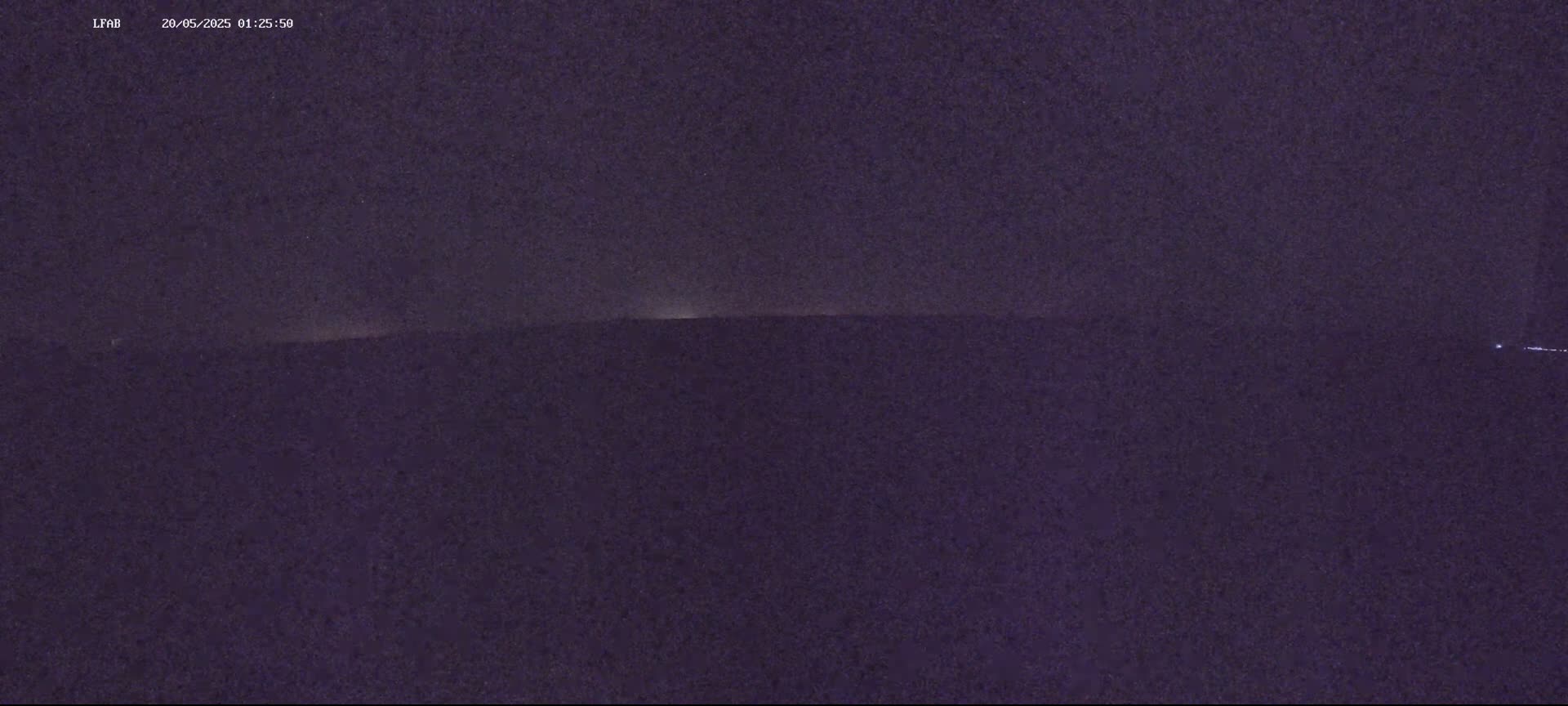 A dark, night-time view of a flat horizon line with a faint glow on the horizon.