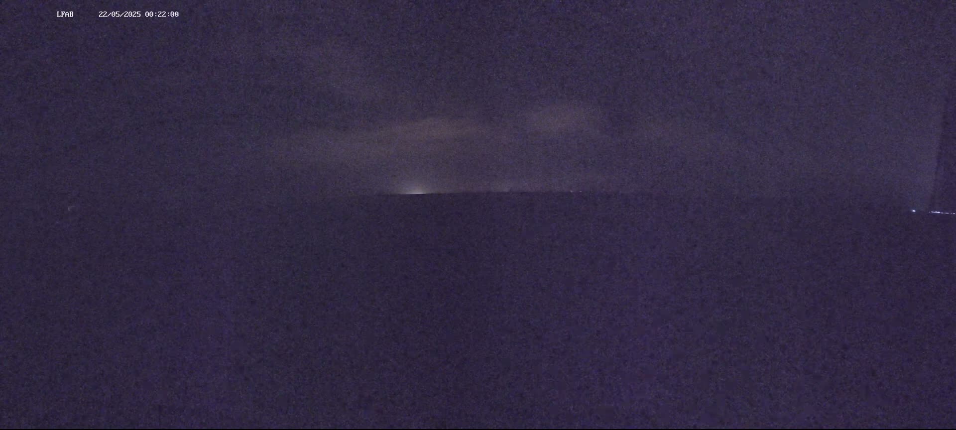 A dark, nighttime scene shows a distant horizon with faint, possibly stormy clouds overhead.