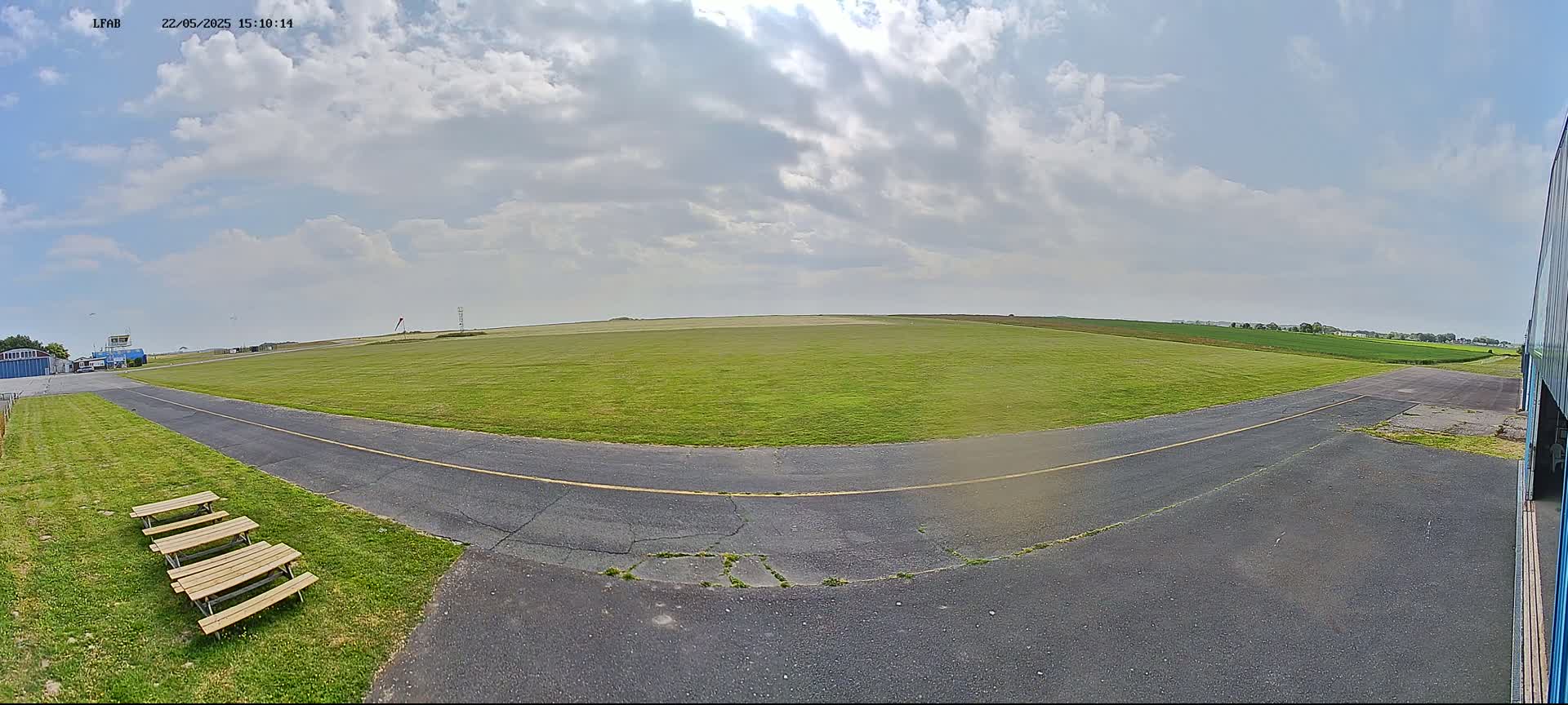 A paved roadway curves around a grassy airfield under a partly cloudy sky.