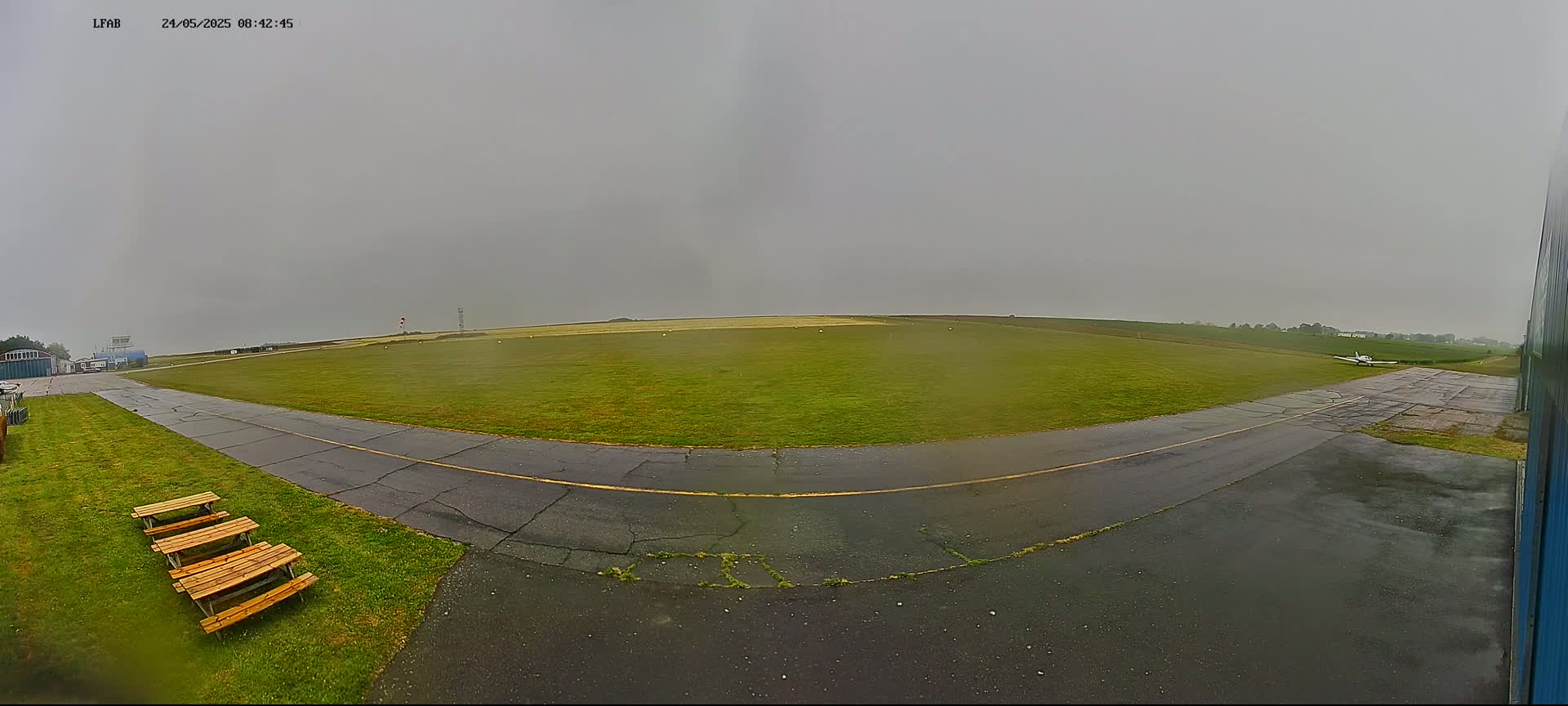 A small airplane sits on a wet grass airfield under an overcast sky.