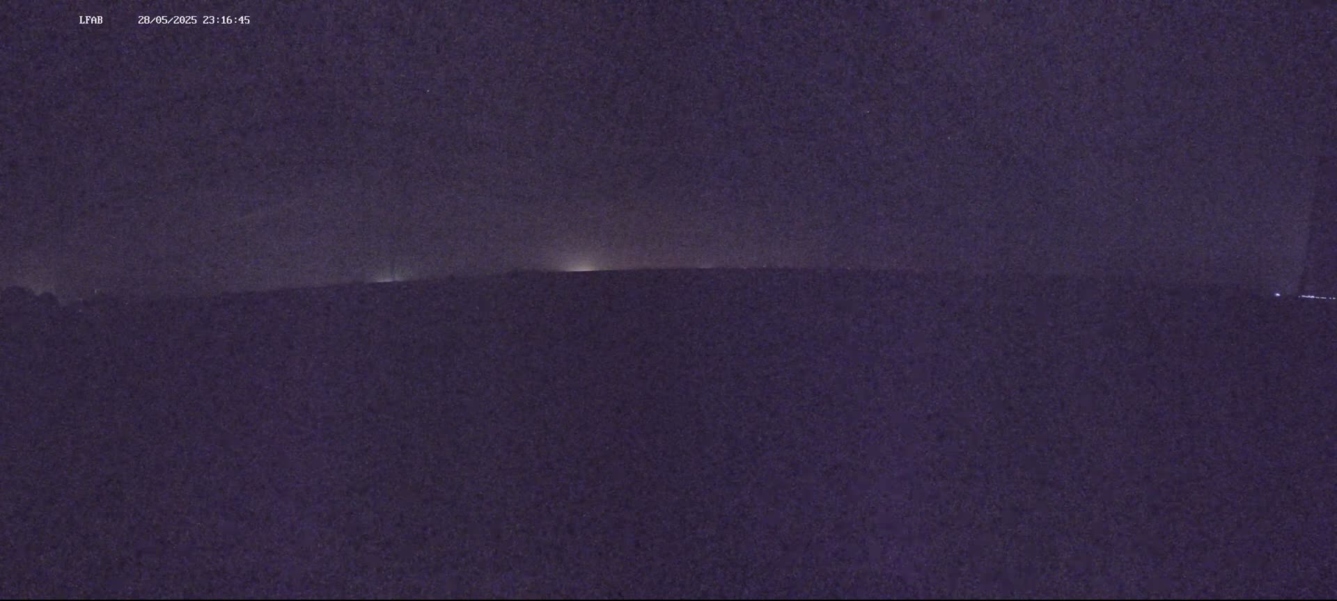 A nighttime, low-light view shows a dark landscape with a faint horizon line illuminated by distant lights.