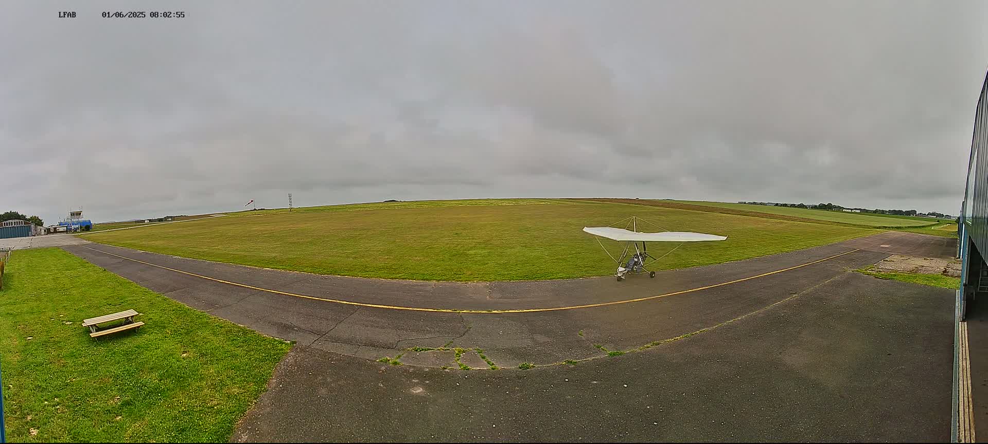 A hang glider sits on a grassy airfield under an overcast sky.