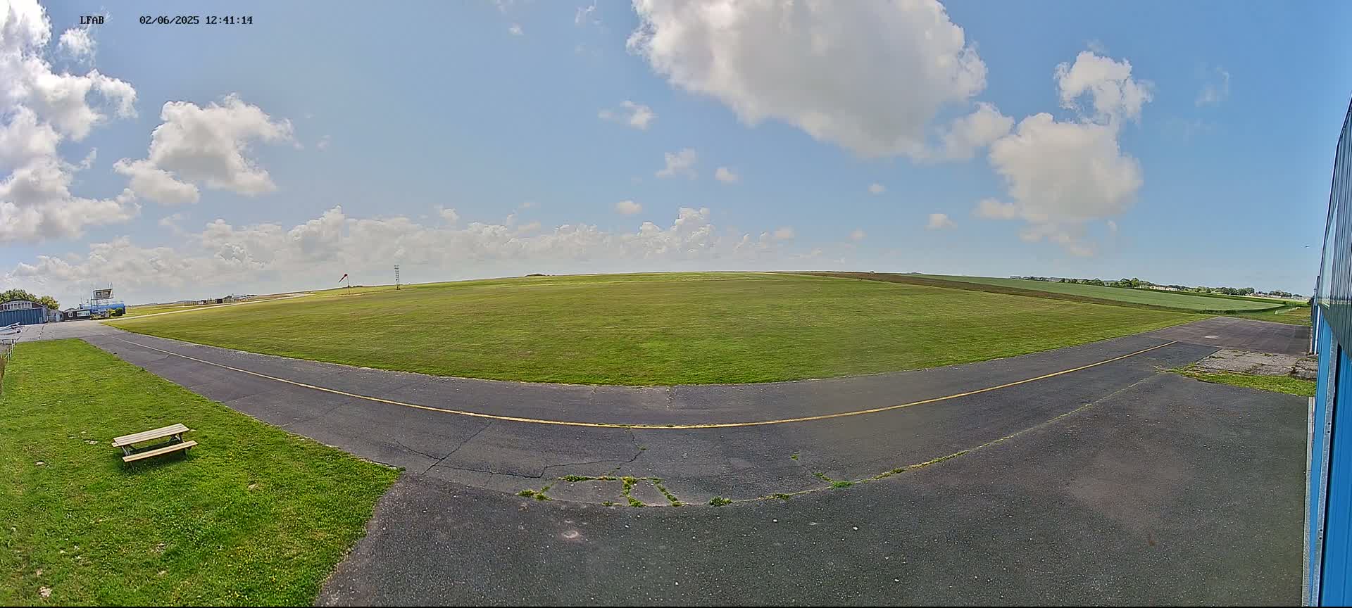 A grassy airfield with a paved taxiway curves into view under a partly cloudy sky.