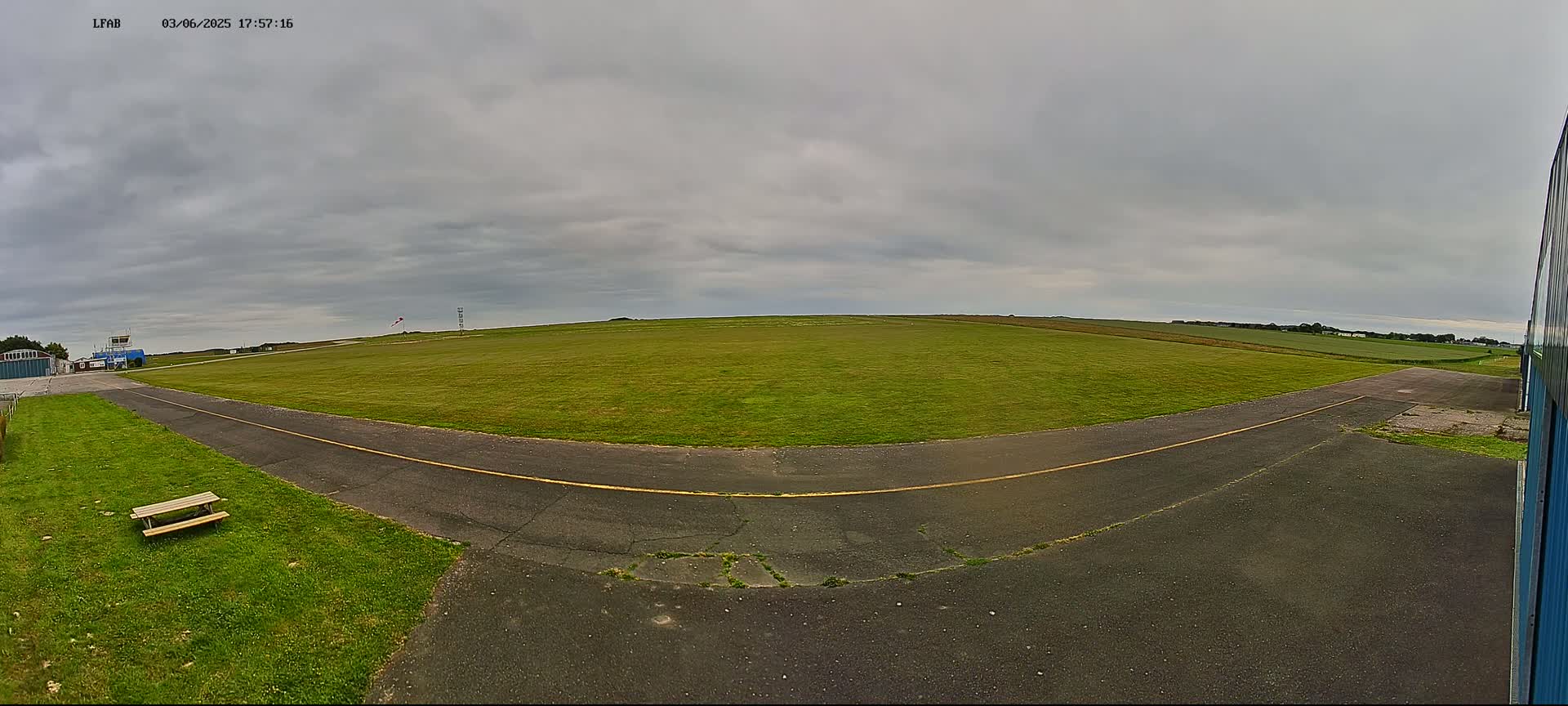A grassy airfield under an overcast sky shows a paved taxiway curving toward a distant horizon.
