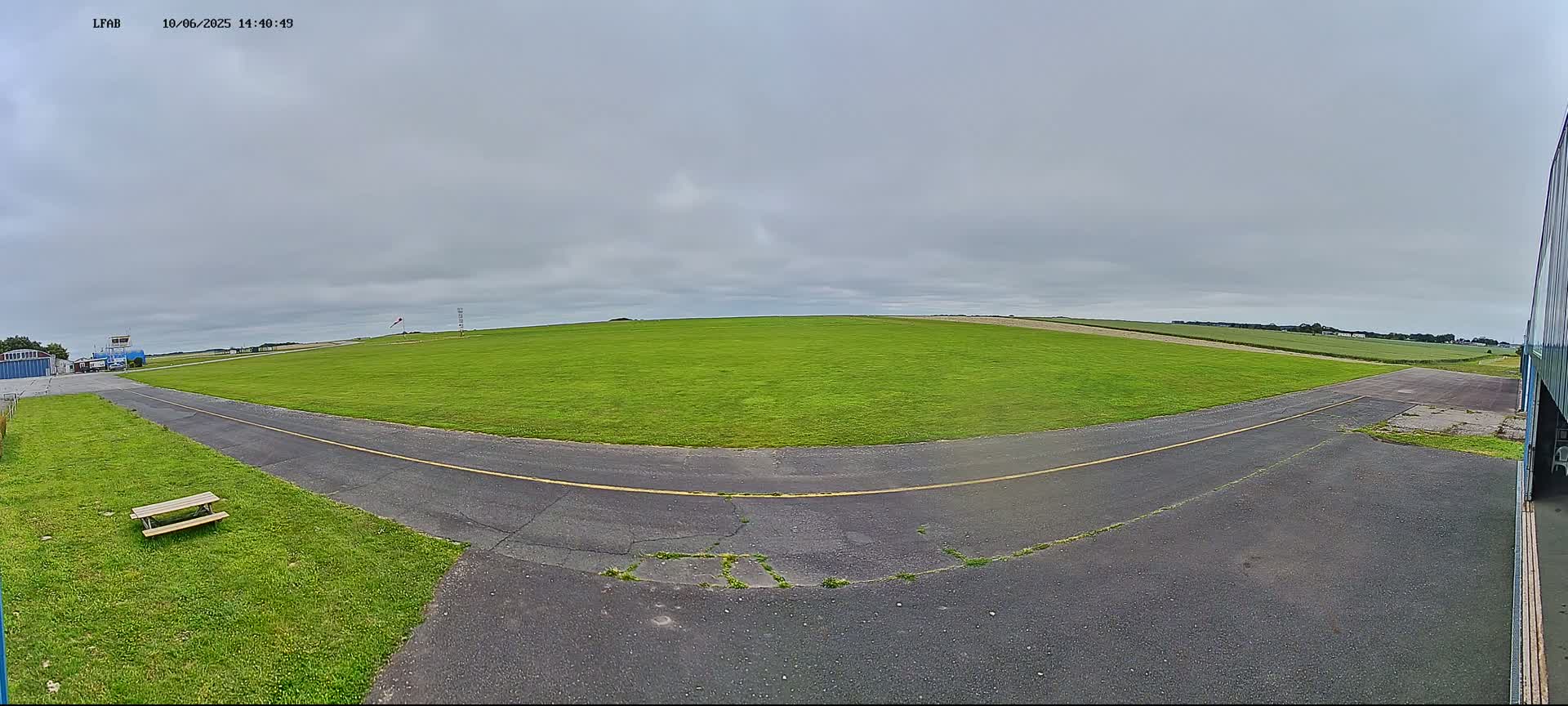 A grassy airfield with a paved taxiway curves toward a control tower under an overcast sky.