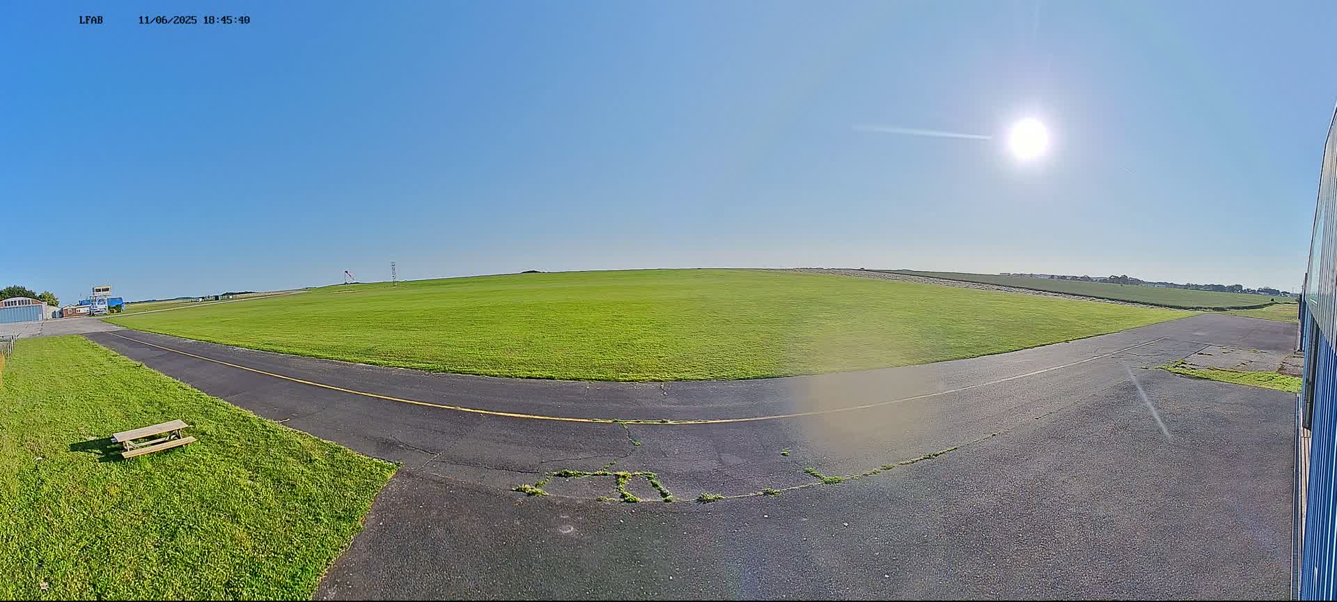 A paved roadway curves around a large grassy field under a bright, sunny sky.