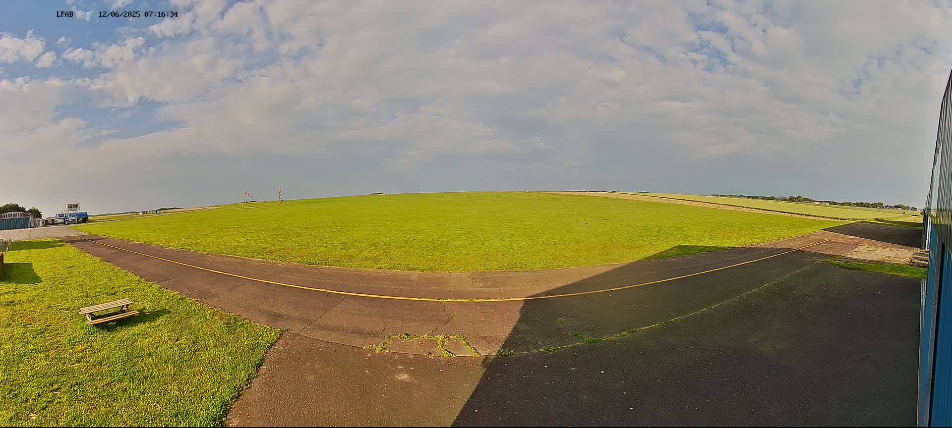 A grassy airfield with a paved taxiway and a partly cloudy sky.