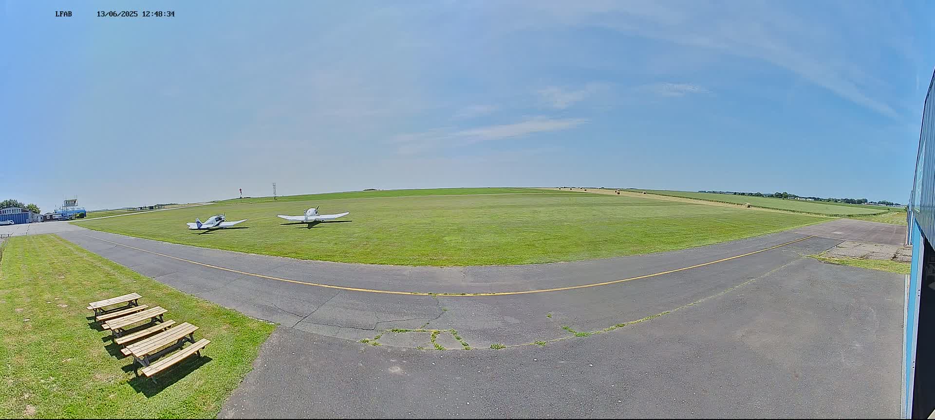 Two small airplanes sit on a grassy airfield under a clear blue sky.