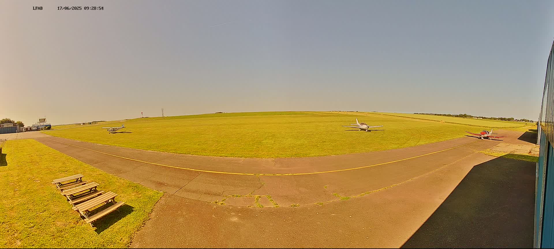Three small airplanes are parked on a grassy airfield under a clear, sunny sky.