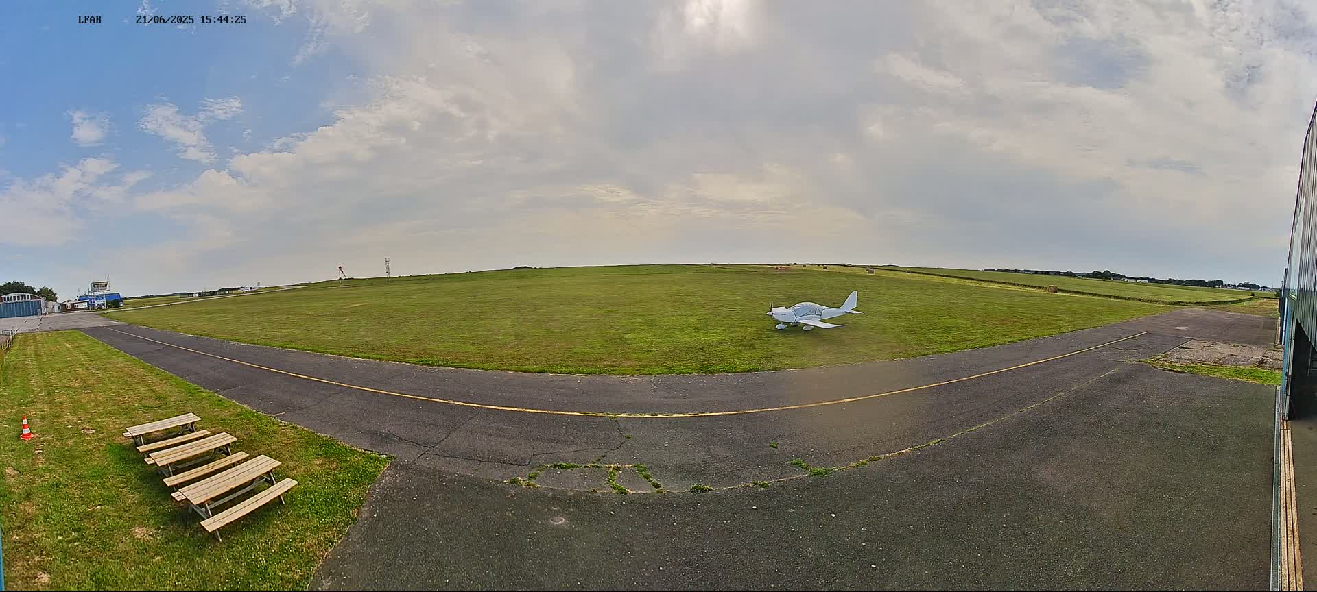 A small, white airplane sits on a grassy airfield under a partly cloudy sky.