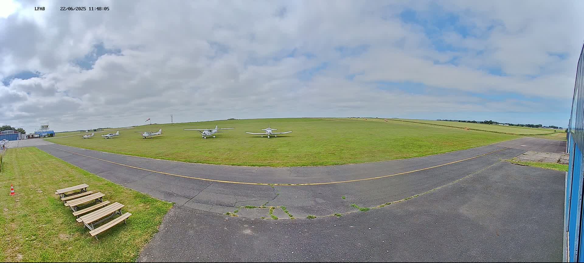 Several small airplanes are parked on a grassy airfield under a partly cloudy sky.