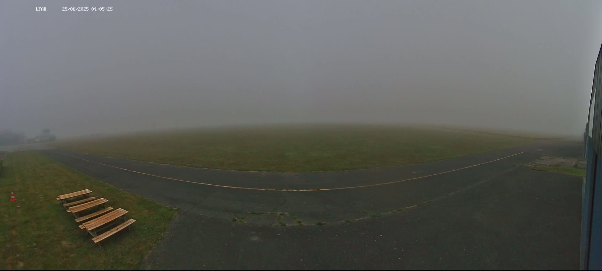 A foggy airfield is shown with a paved road and several wooden picnic tables.