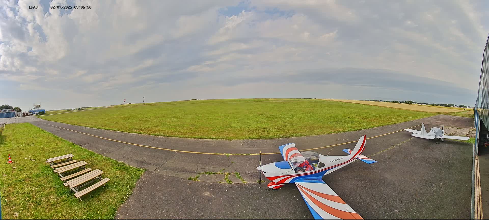 Two small airplanes are parked on a grassy airfield under a partly cloudy sky.