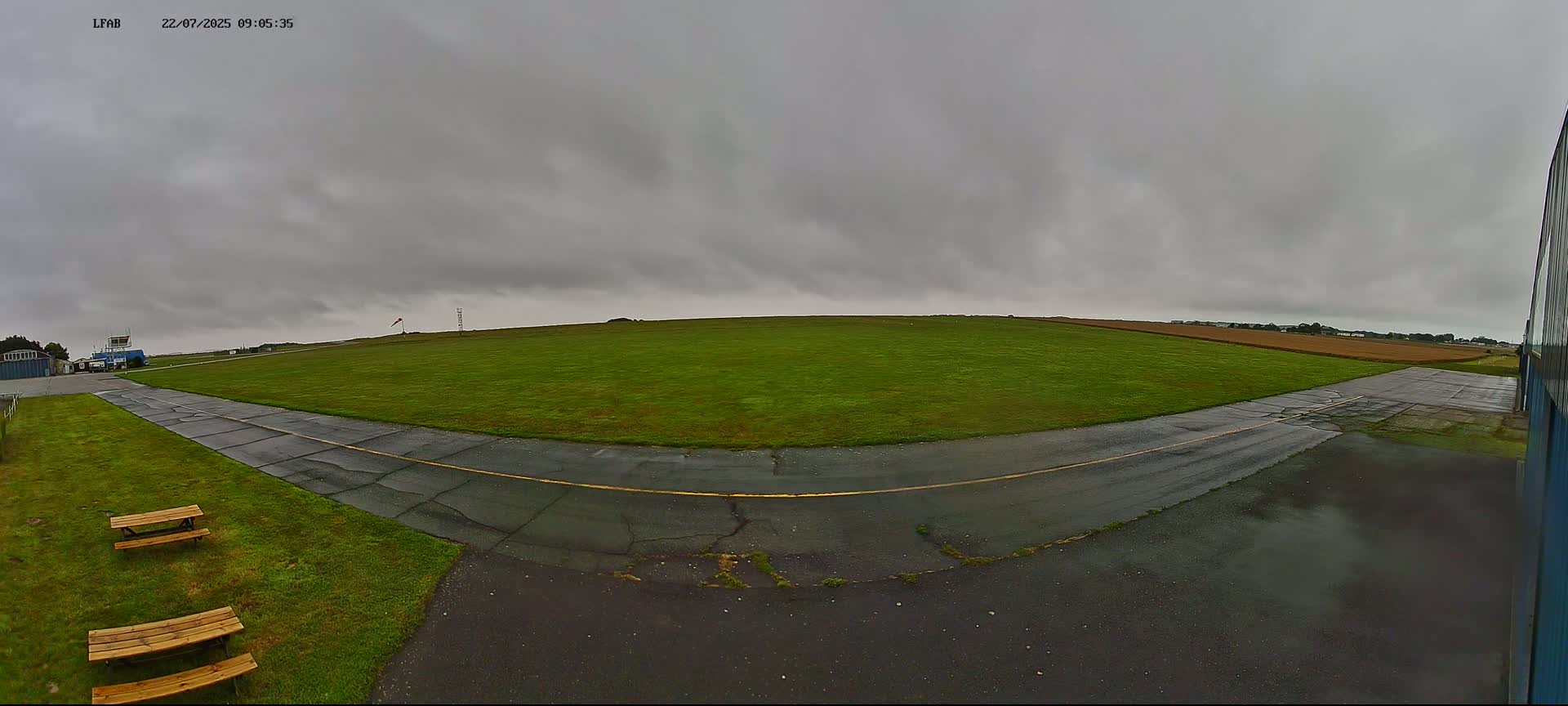 A grassy airfield with a paved taxiway is visible under an overcast sky.