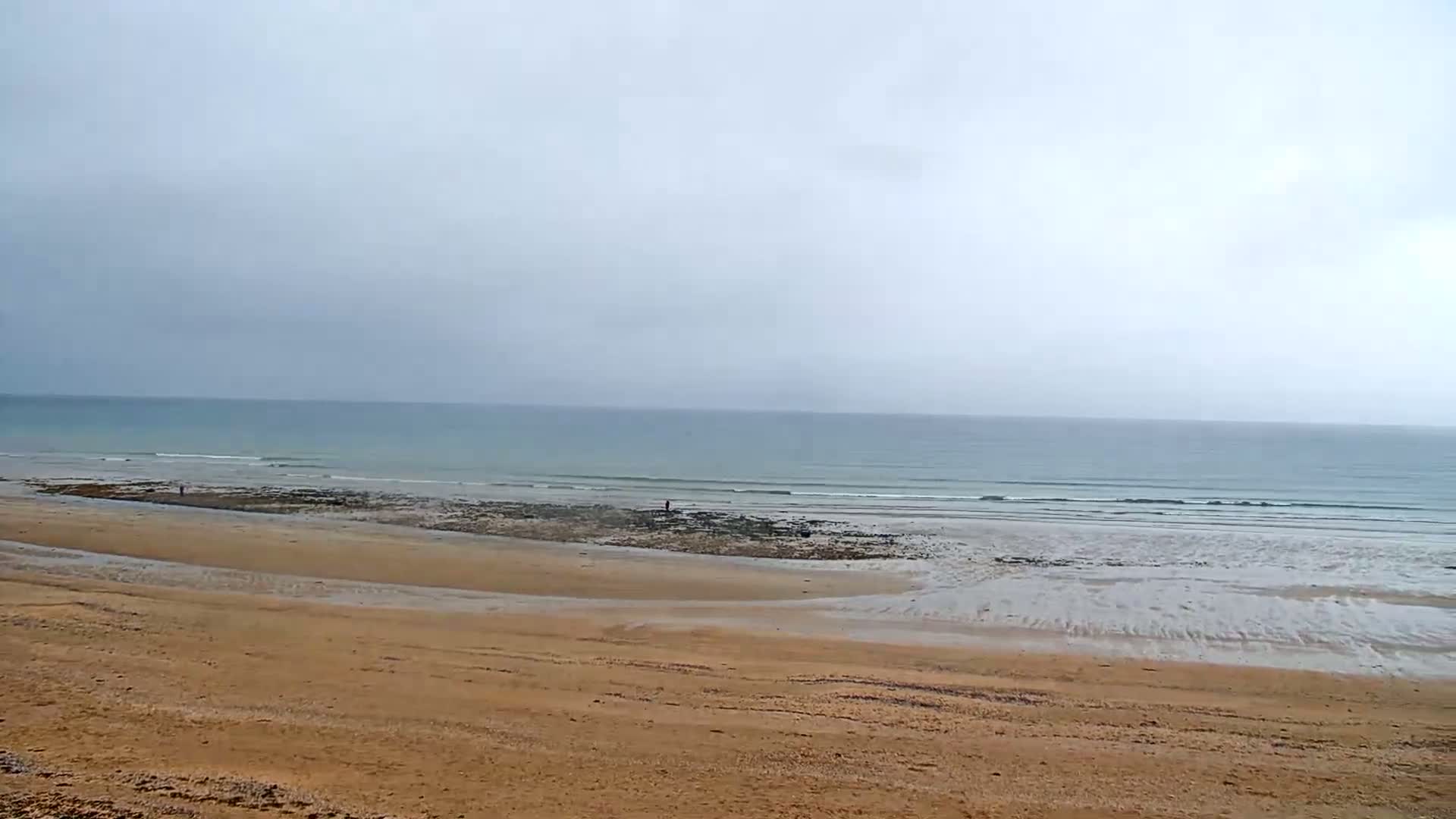 A sandy beach stretches to a calm, light-blue ocean under an overcast sky.