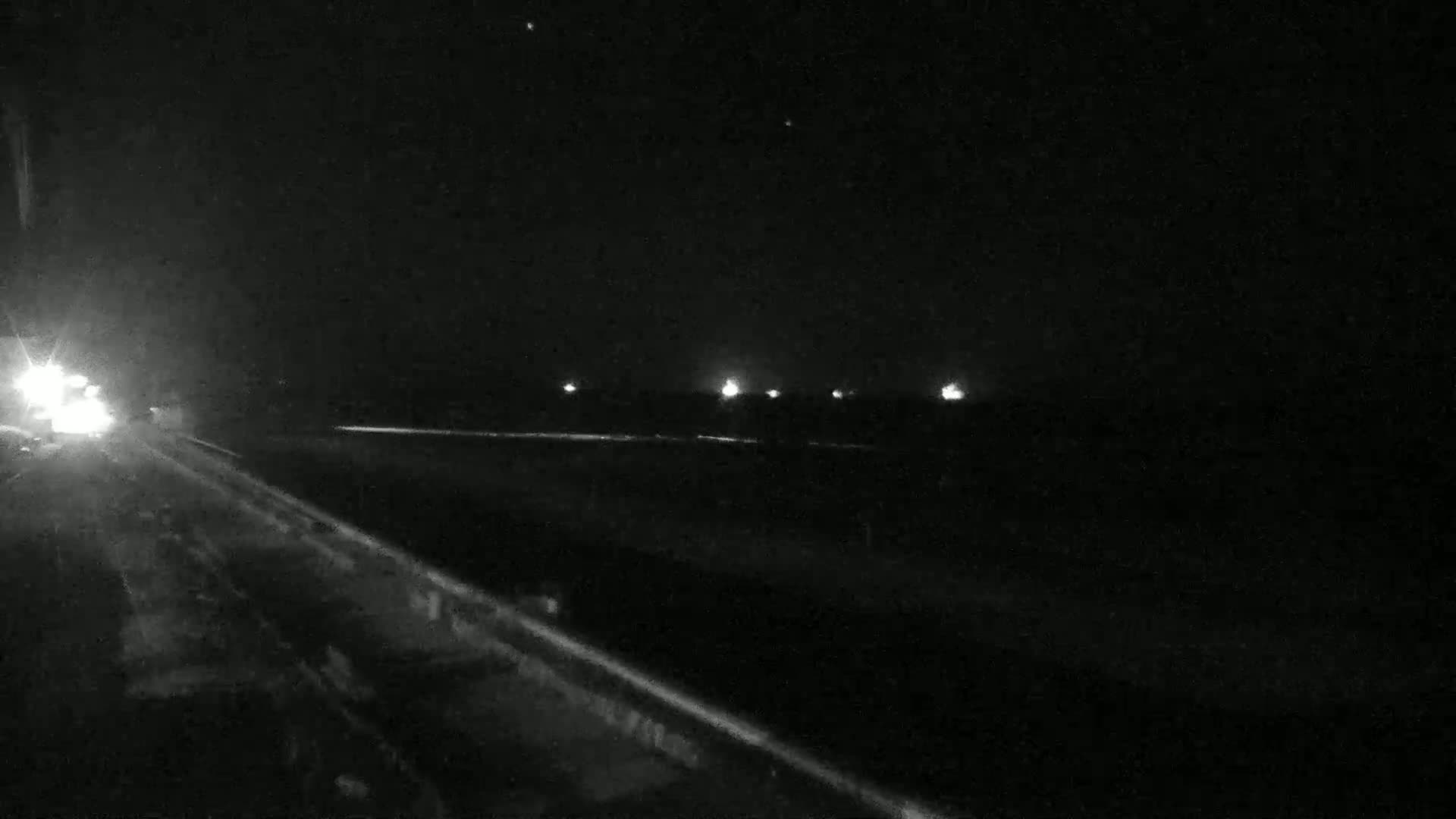 A dark, nighttime highway scene shows a few distant lights and a vehicle's headlights approaching in the foreground.
