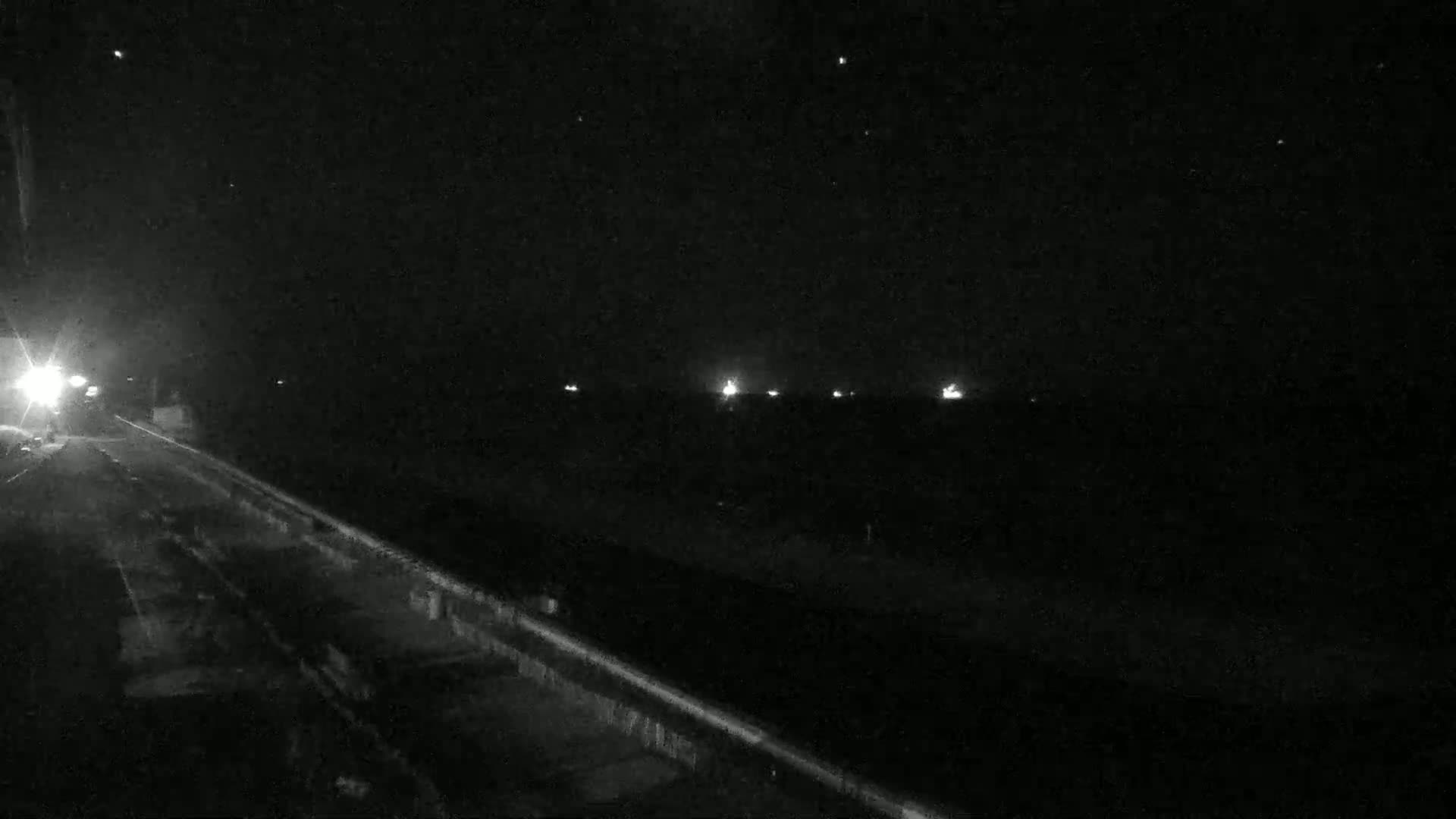 A nighttime view of a dark road with a few distant lights and a vehicle's headlights visible in the foreground.