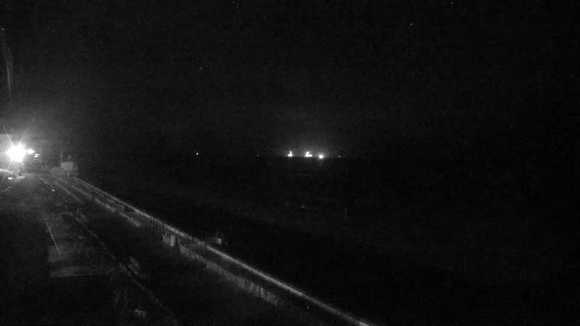A nighttime view of a roadway leading towards distant lights under a dark sky.