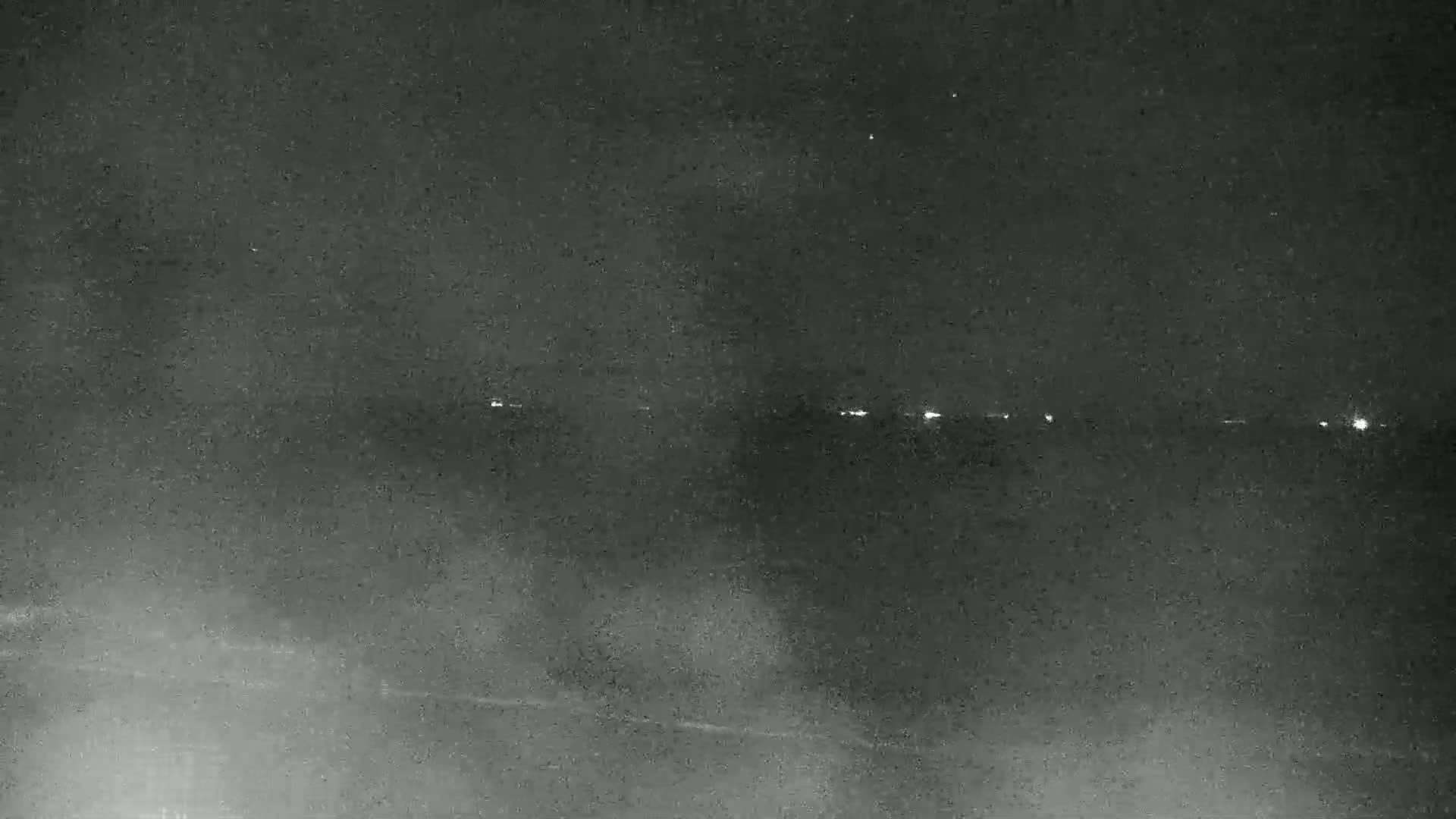 A nighttime, hazy, or foggy scene shows a distant line of lights on the horizon.