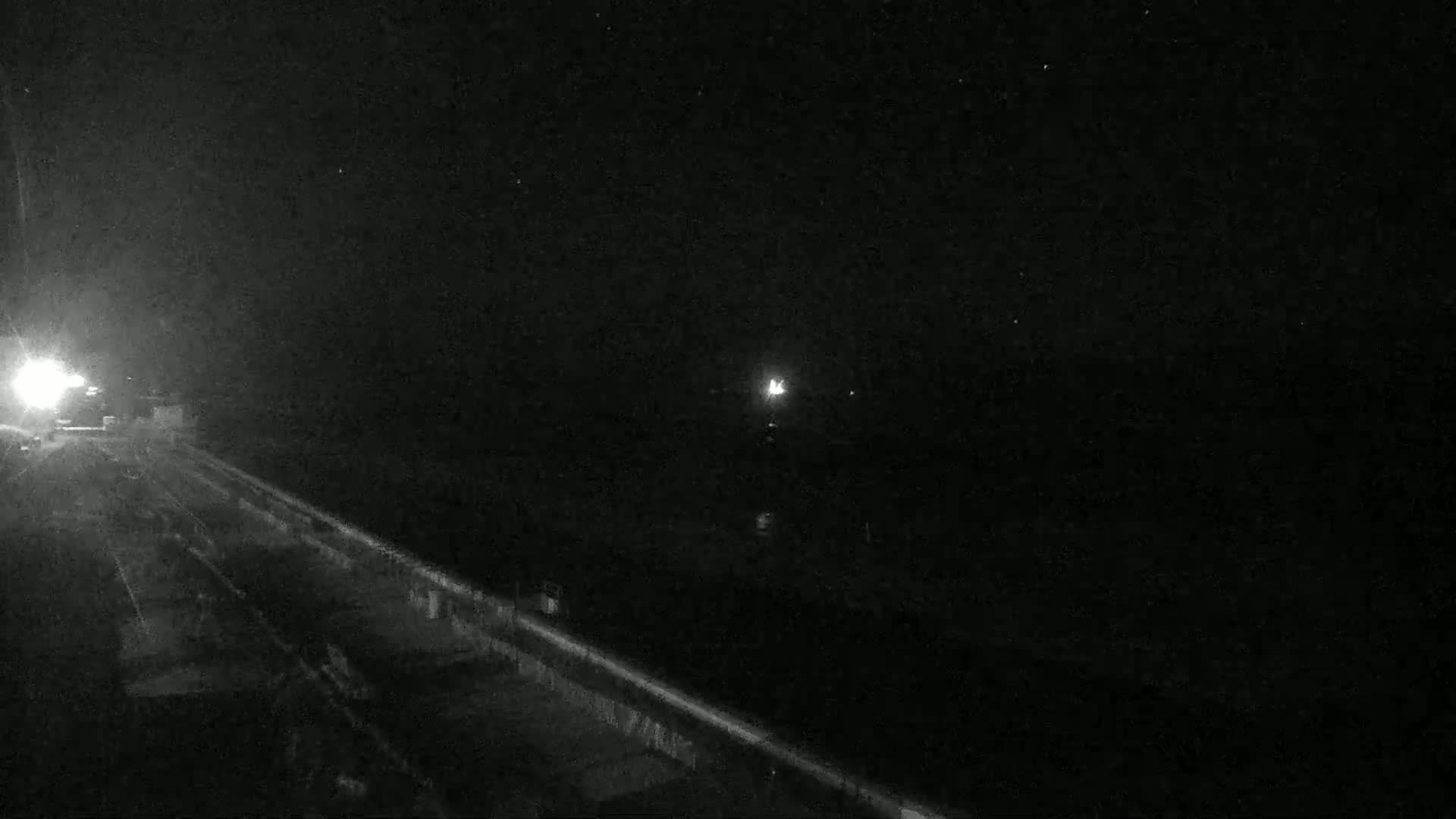 A nighttime, low-light view shows a dark road and a body of water, with a faint light visible in the distance.