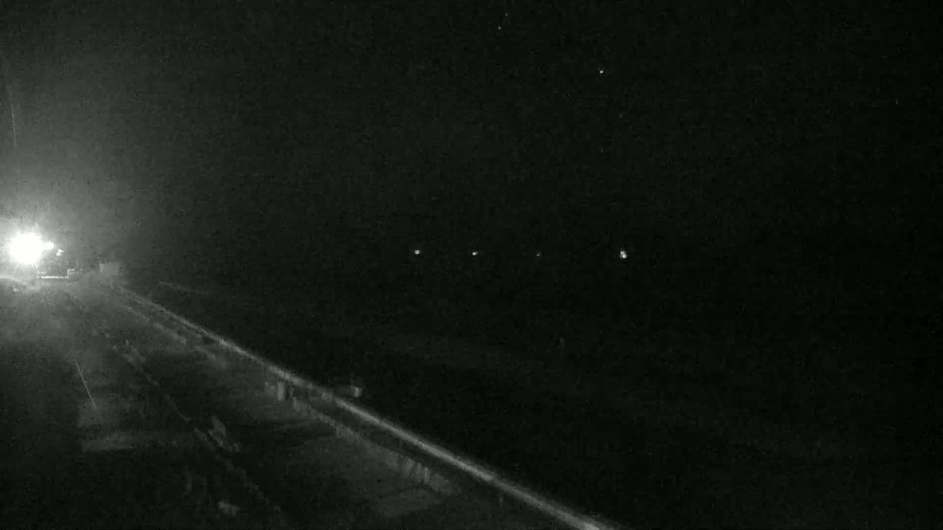A nighttime view of a roadway with a few distant lights under a dark, clear sky.