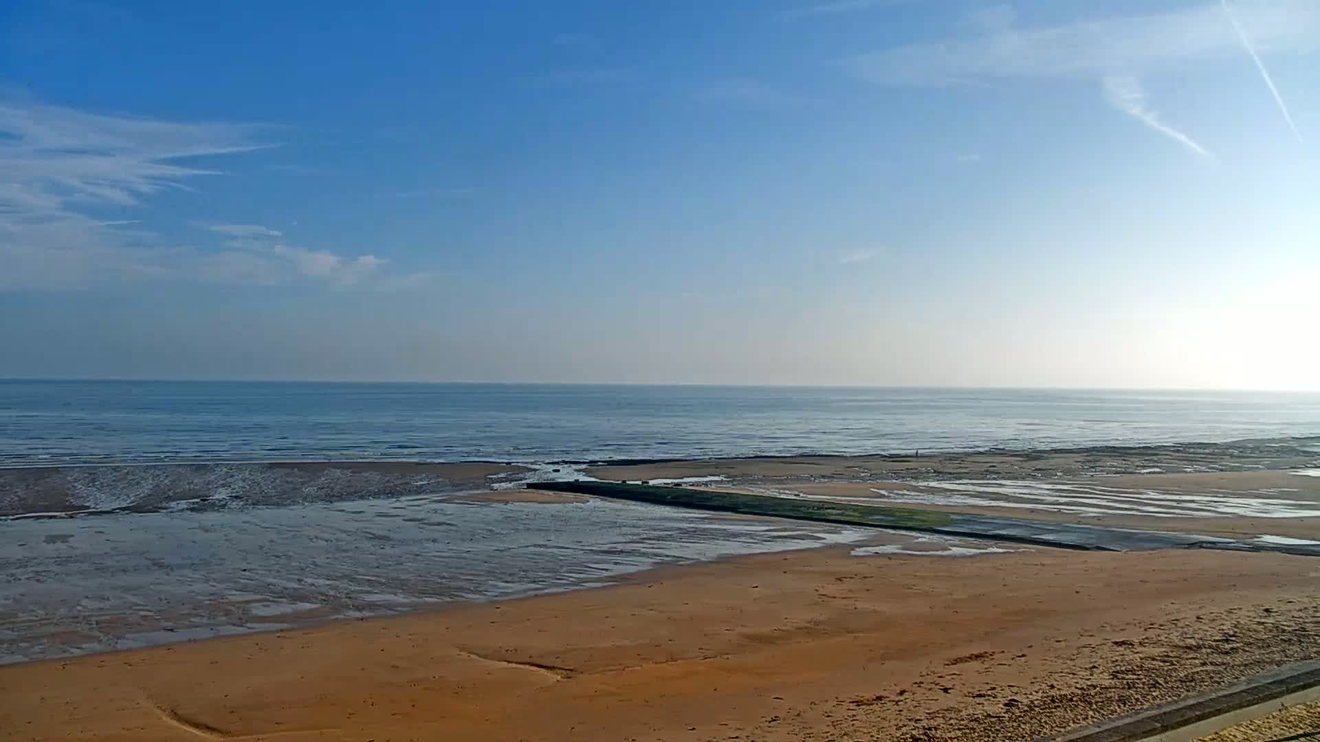 A sandy beach stretches out to a calm ocean under a mostly clear blue sky.
