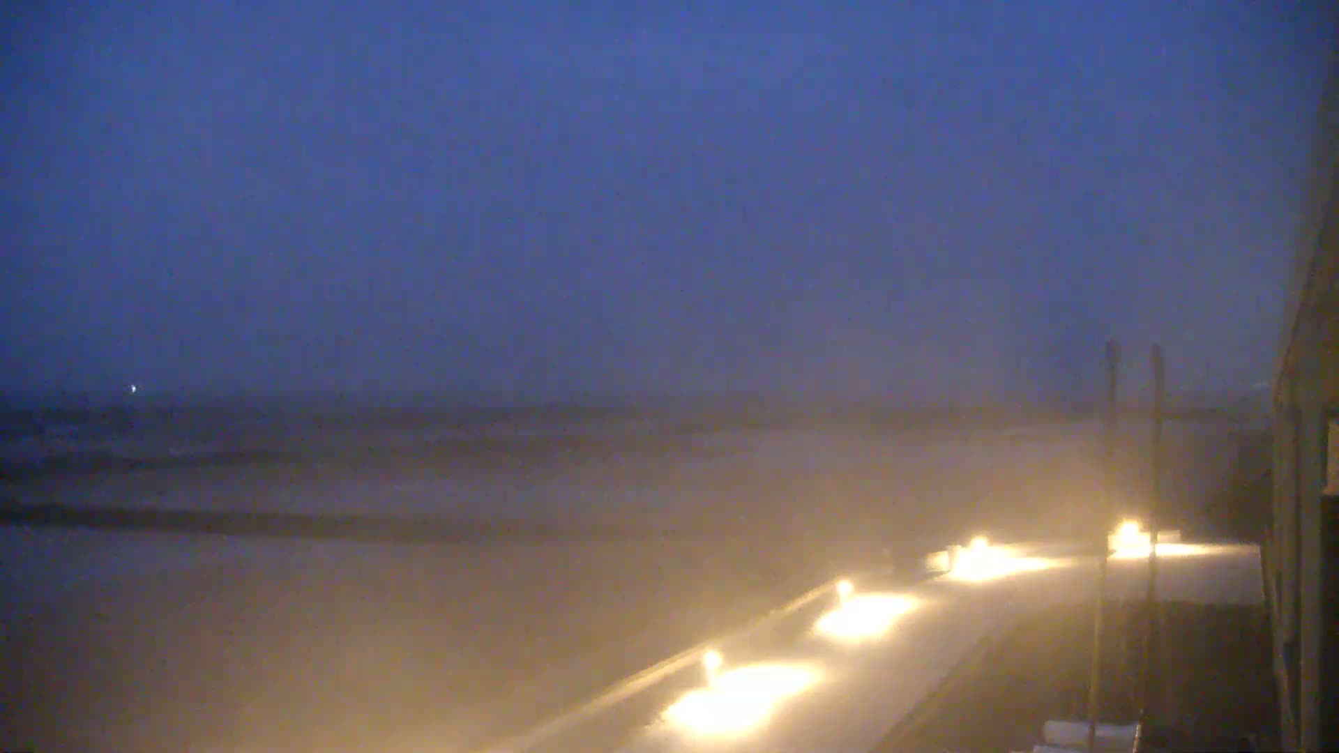 A hazy, dark-blue twilight scene shows a long, dimly lit walkway extending toward a beach under a dusky sky.
