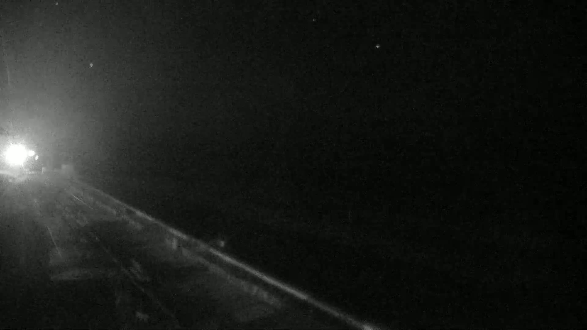 A nighttime view of a road with headlights in the distance under a dark, clear sky.