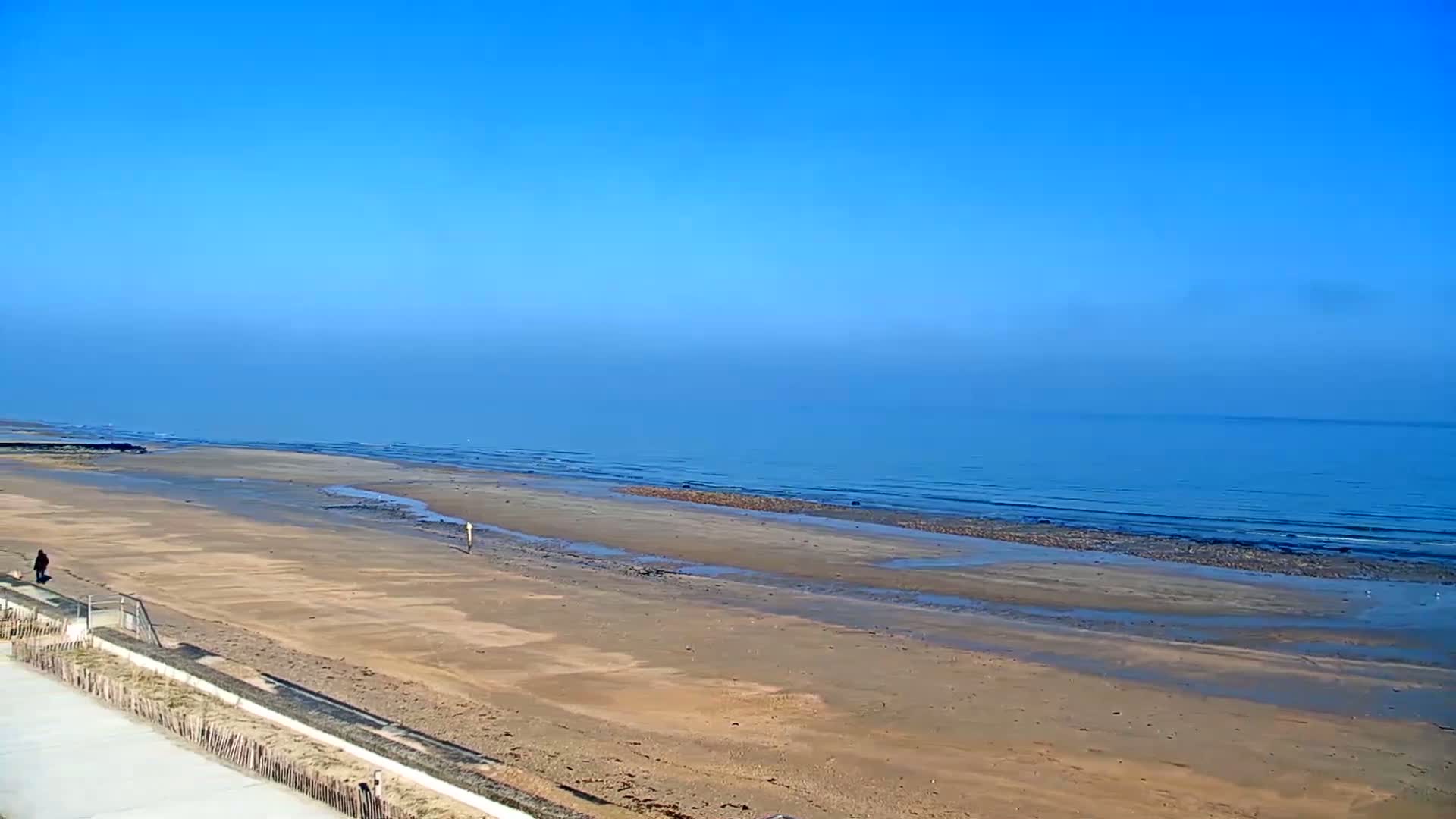 A wide sandy beach stretches to a calm, blue ocean under a clear blue sky.