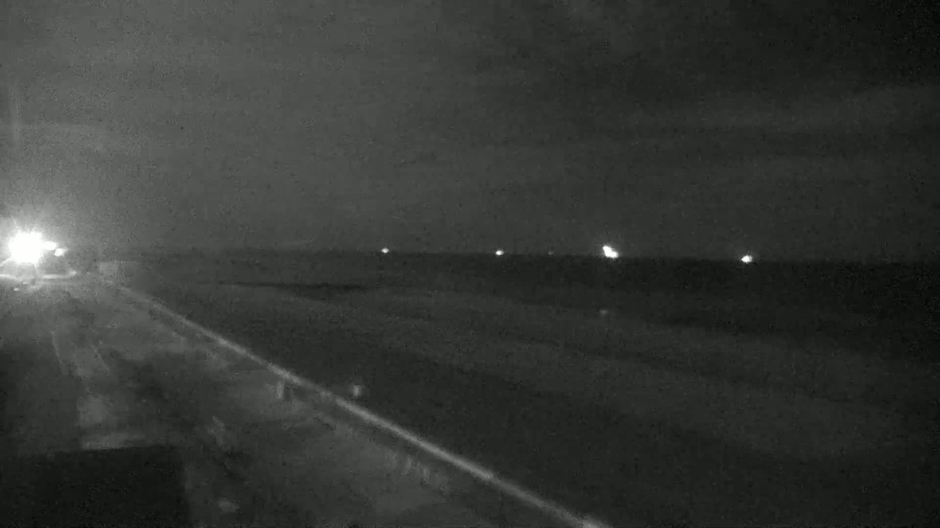 A dark, nighttime view of a highway with a few distant lights visible, under a cloudy sky.