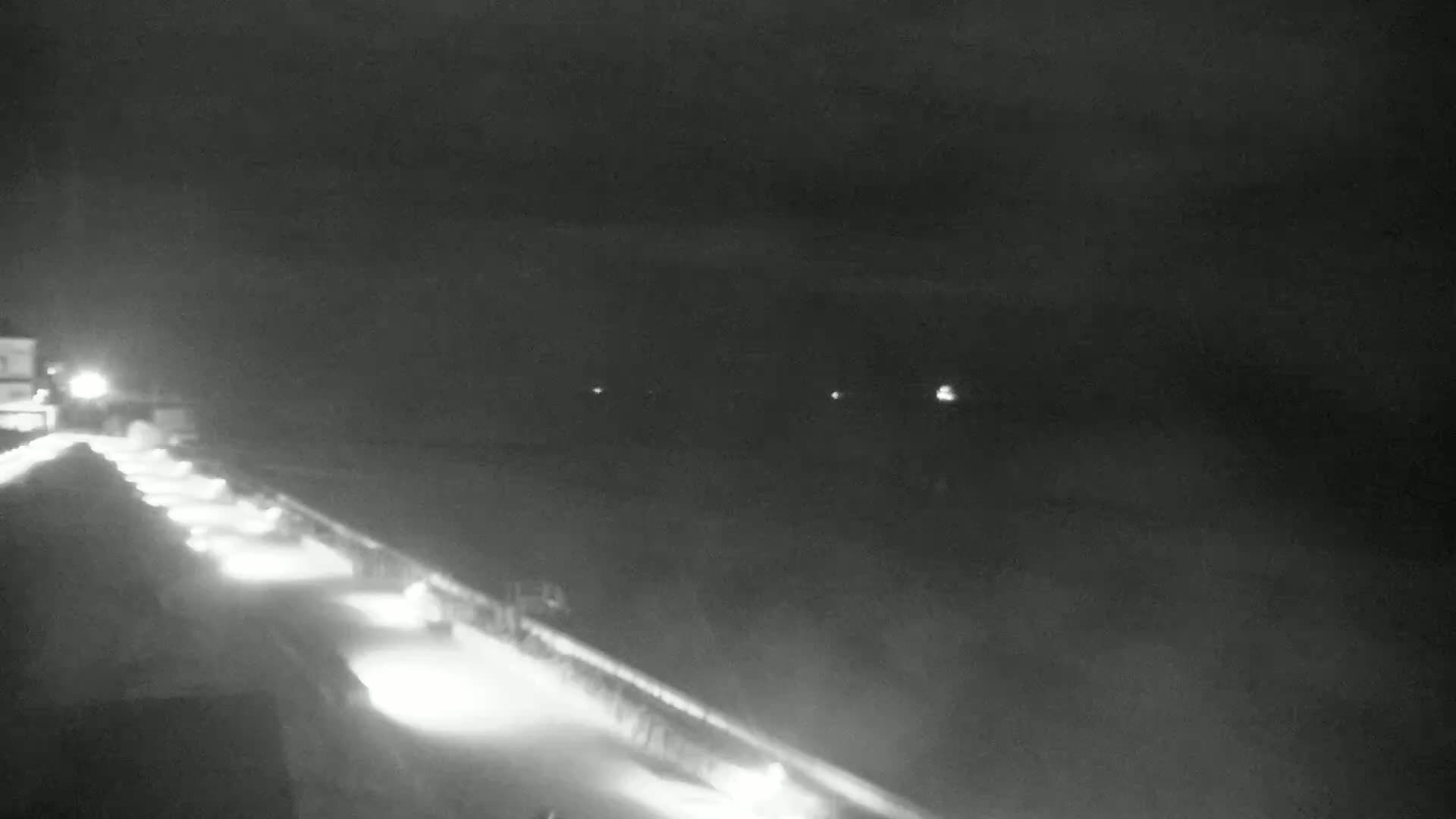 A nighttime, hazy view shows a snow-covered road with lights lining the side, and distant lights faintly visible in the darkness.