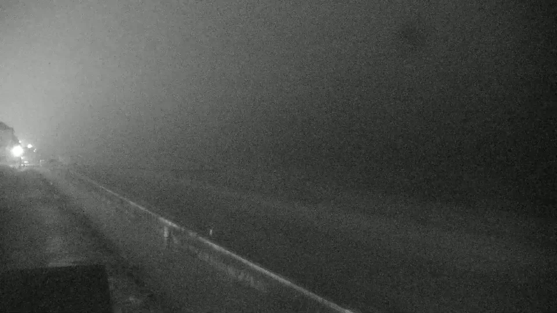 A nighttime, foggy view of a road with a few vehicles visible in the distance.
