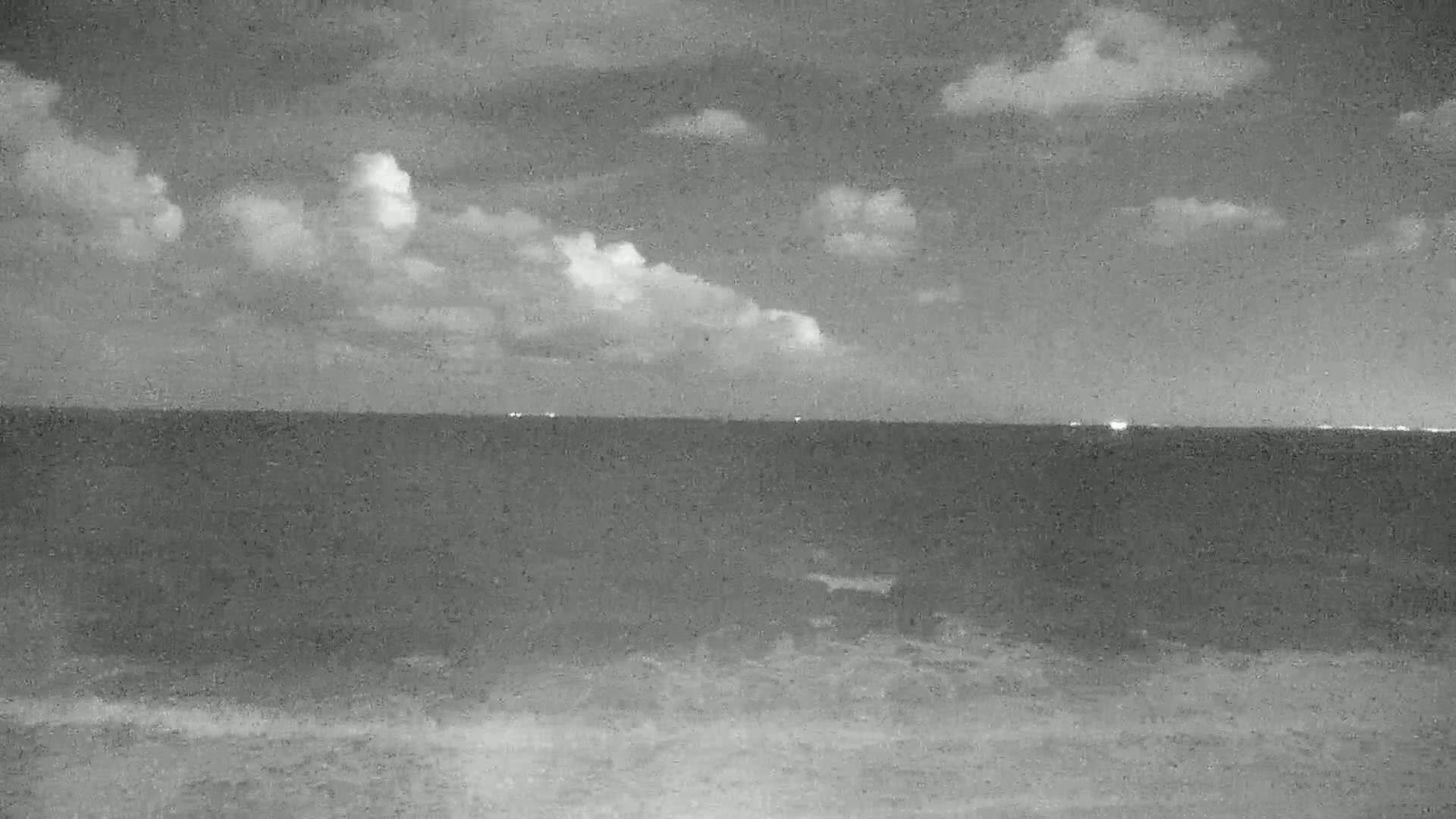 A mostly cloudy night scene shows a dark ocean with a faint shoreline at the bottom.