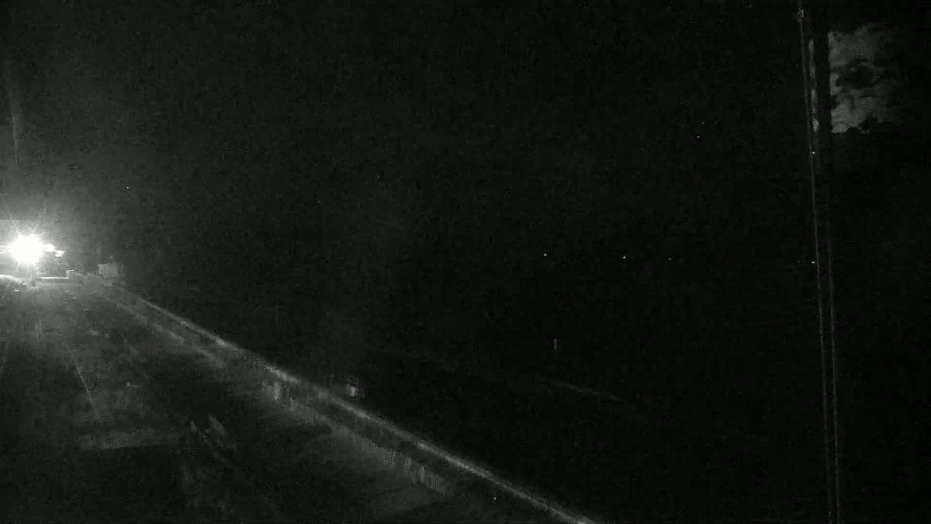 A nighttime view of a highway with a vehicle's headlights visible in the distance.