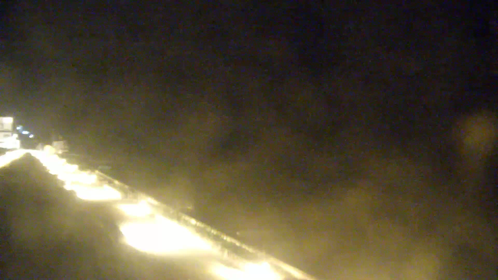 A nighttime aerial view shows a highway with a line of headlights from vehicles traveling in the same direction.