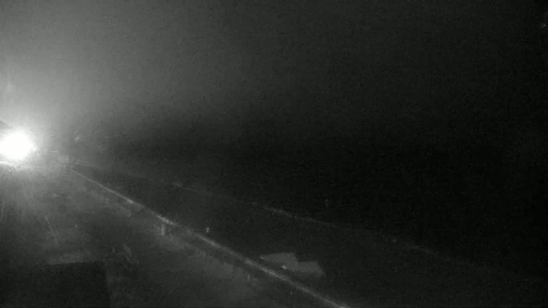 A foggy night scene shows a dark highway with a few vehicle headlights visible in the distance.