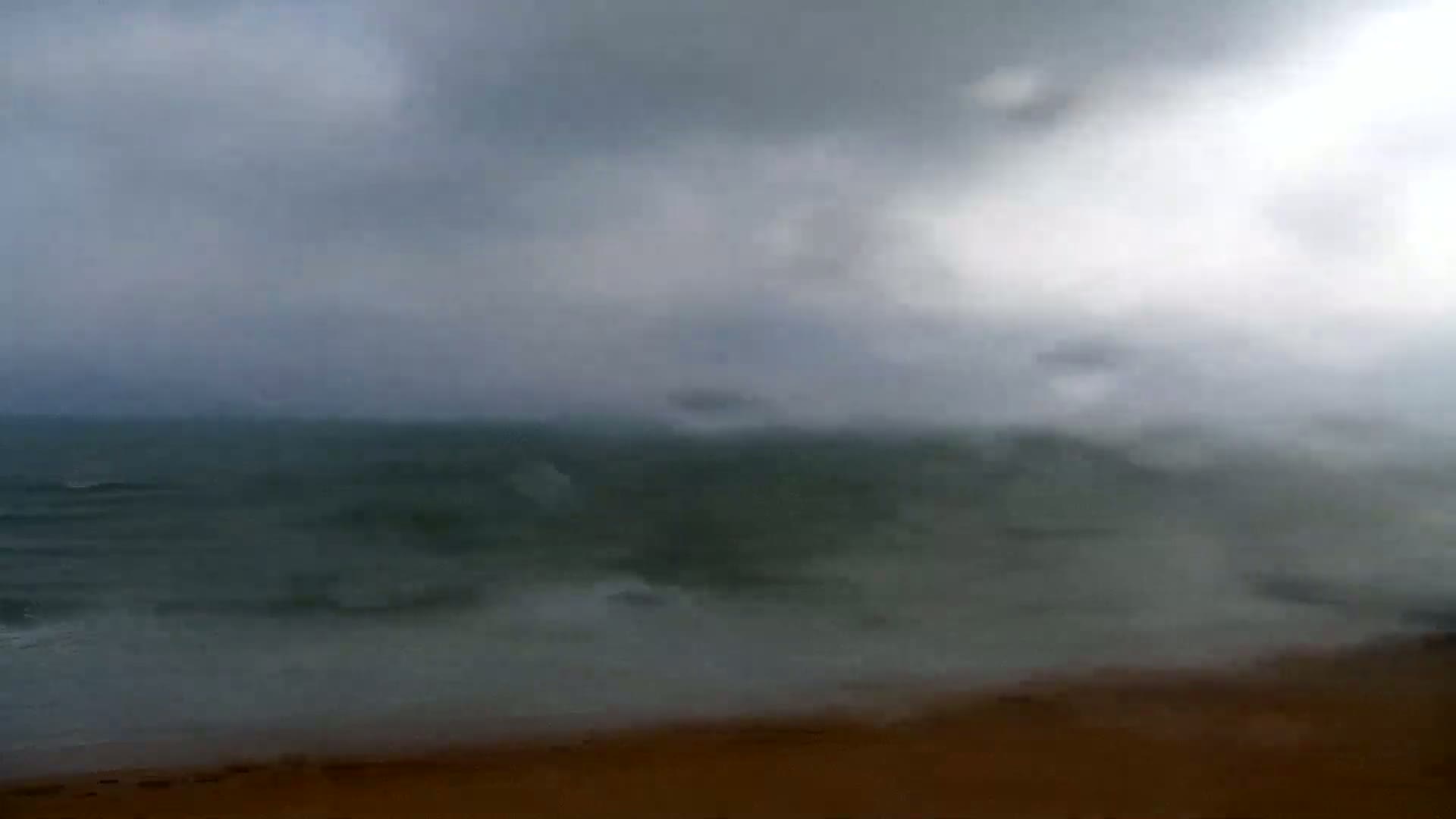 A grey, overcast sky hangs over a dark, choppy sea meeting a sandy beach.