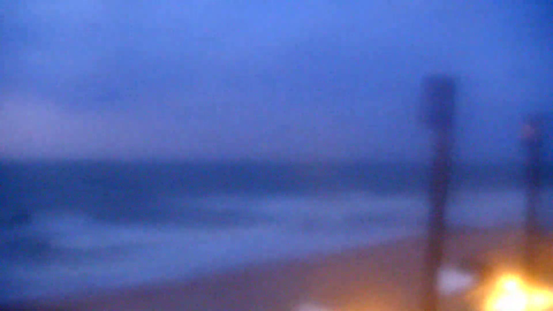 A blurry image shows a dark, wavy ocean under a twilight sky, with indistinct objects in the foreground.